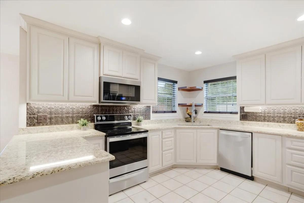 Well-appointed kitchen featuring white cabinetry, light-toned granite countertops, and a decorative tile backsplash.