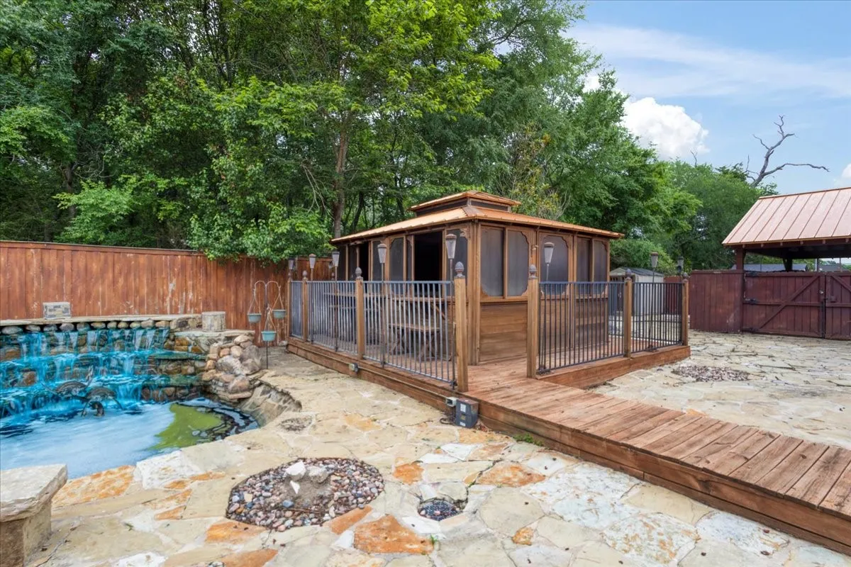Stone patio featuring a spa room, built-in waterfall, and wood fencing.
