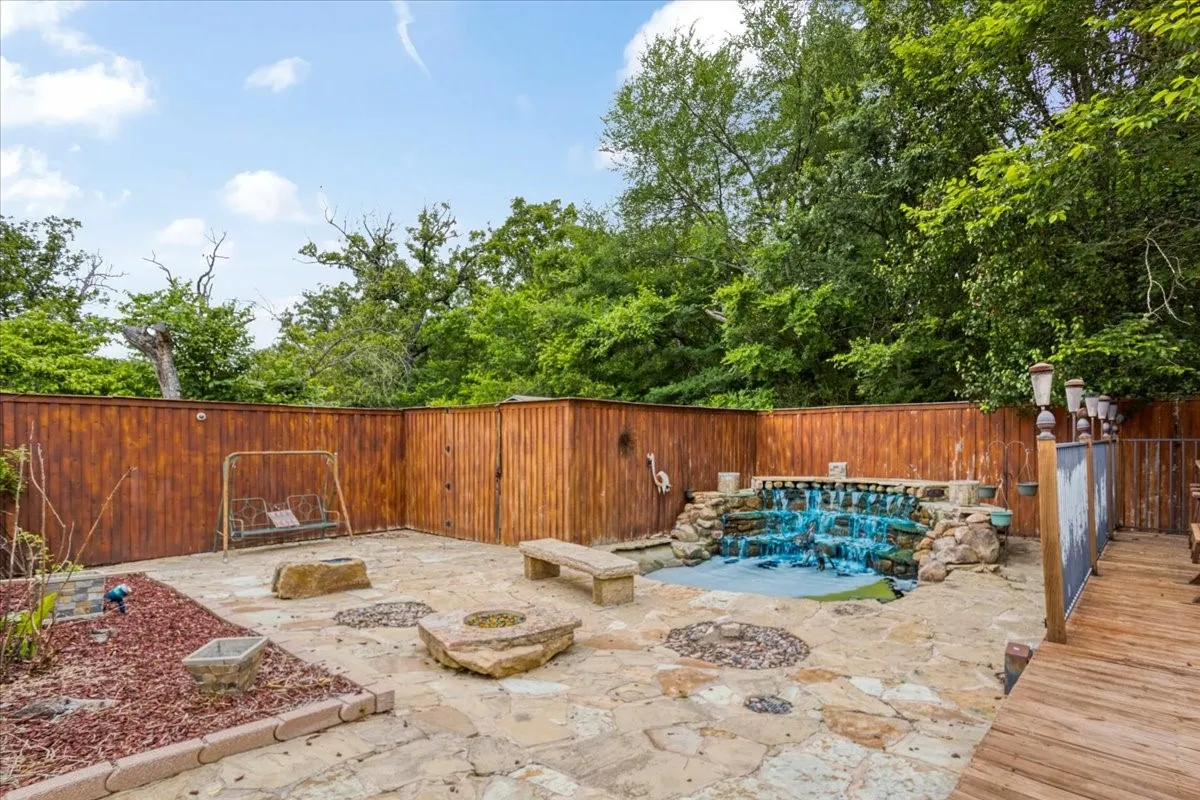 Stone patio featuring a built-in waterfall, fire pits, and wood fencing.