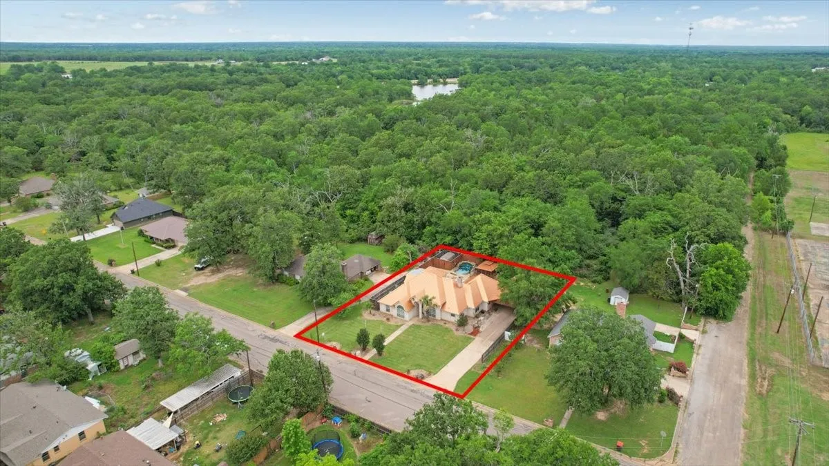 Aerial property overview featuring a prominent main residence with a beige exterior, a multi-car driveway, and mature landscaping