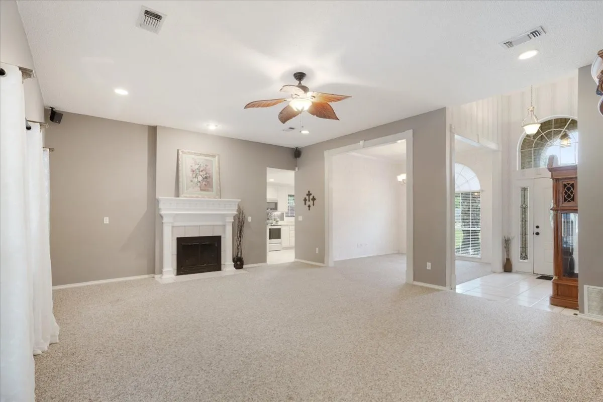 Spacious living area featuring a fireplace with a white mantel, recessed lighting, and a ceiling fan.
