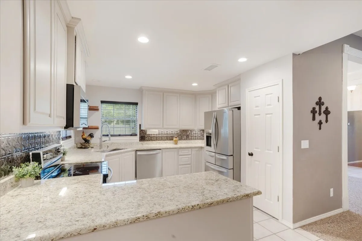 Kitchen featuring light-colored cabinetry, stainless steel appliances, a tile backsplash, light-toned granite countertops, and recessed lighting.