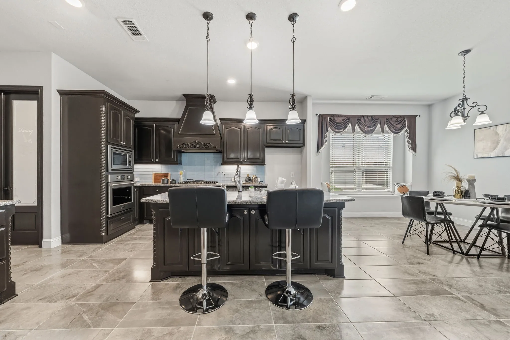 Expansive kitchen featuring dark wood cabinetry, a central island with countertop seating, and integrated stainless steel appliances