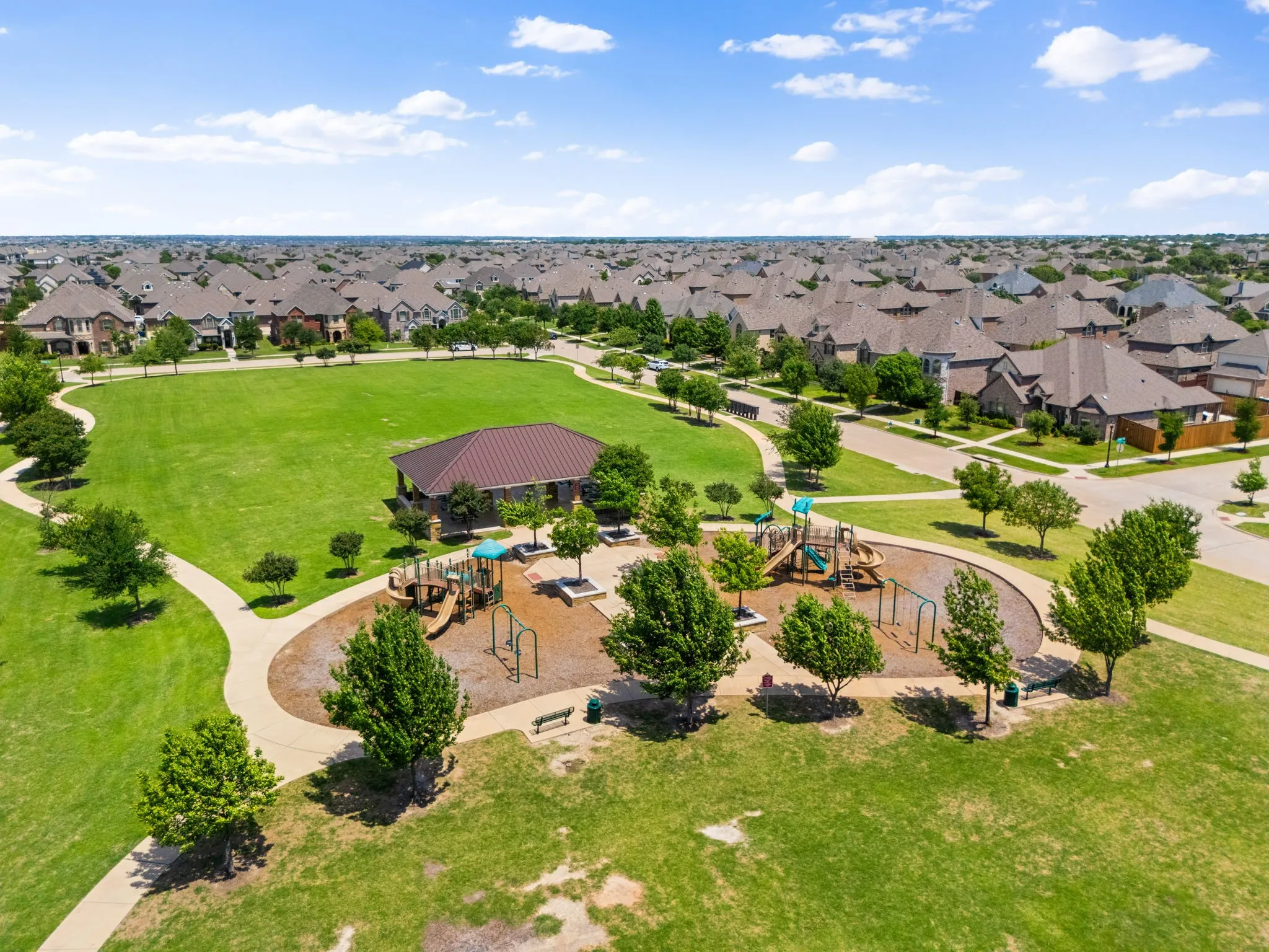 Expansive green space featuring a playground, paved walking paths, and a covered pavilion