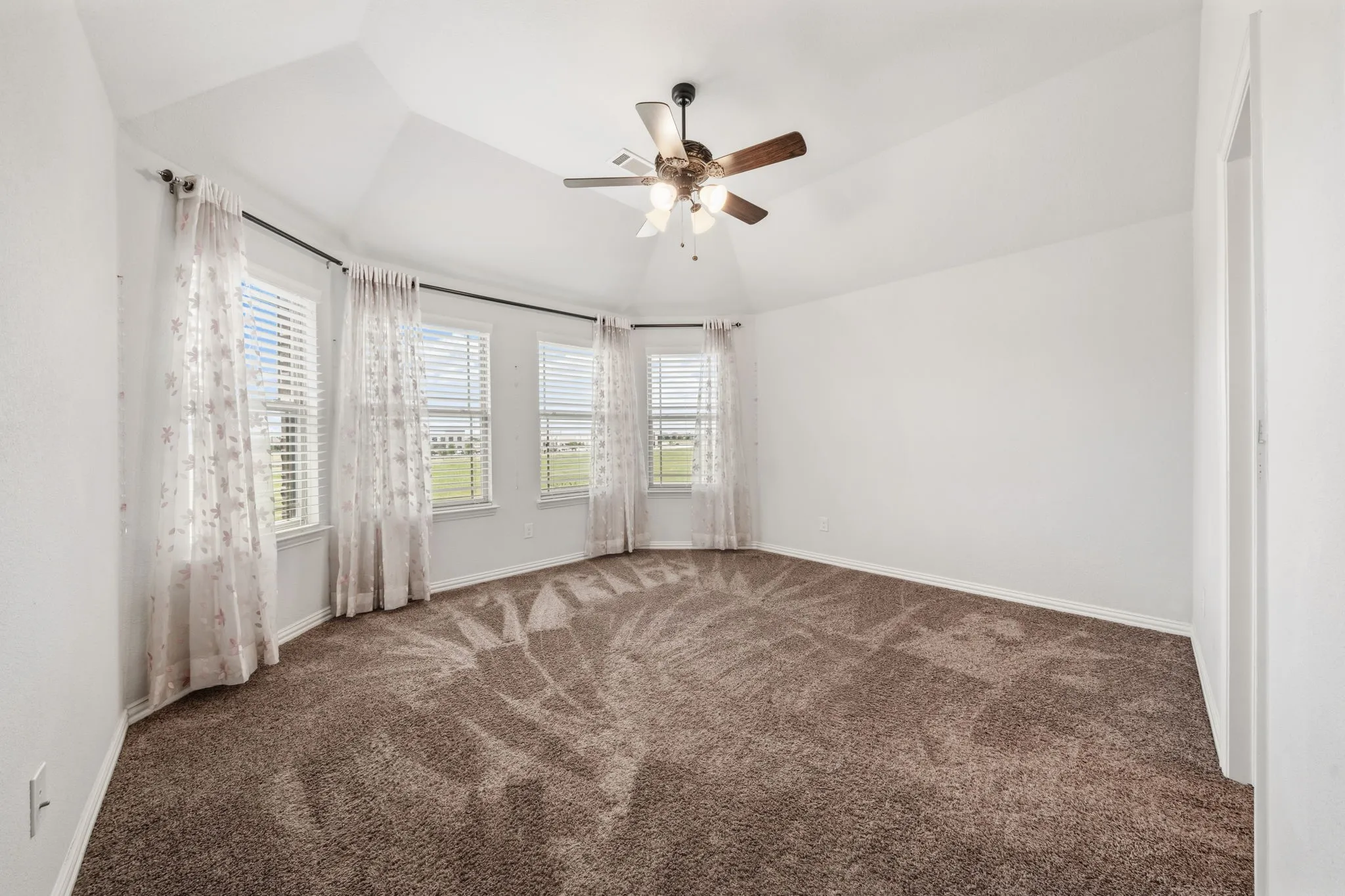 Expansive room featuring a vaulted ceiling and a ceiling fan with integrated lighting