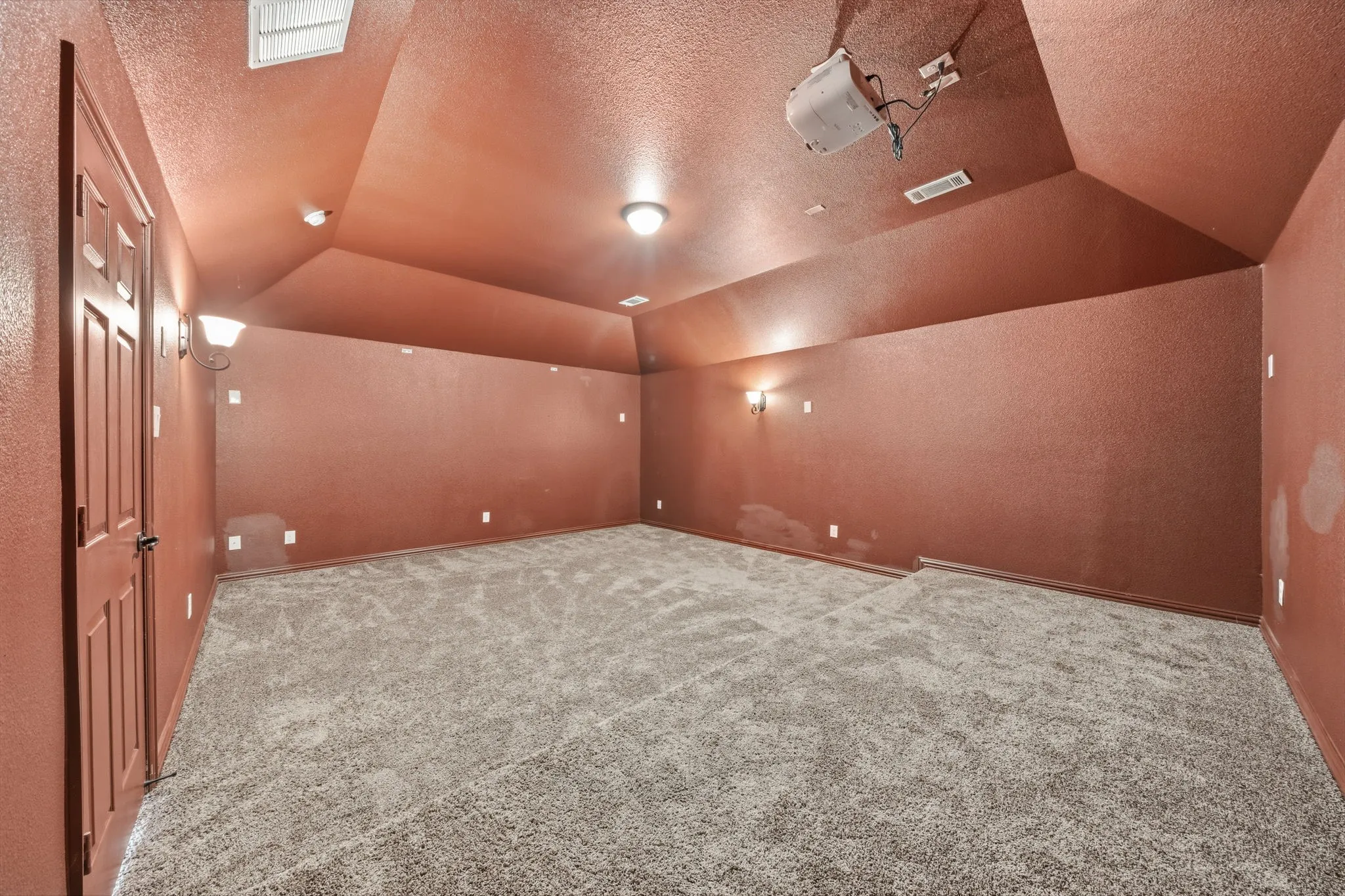 Carpeted room featuring a ceiling-mounted projector, multiple wall sconces, and recessed lighting