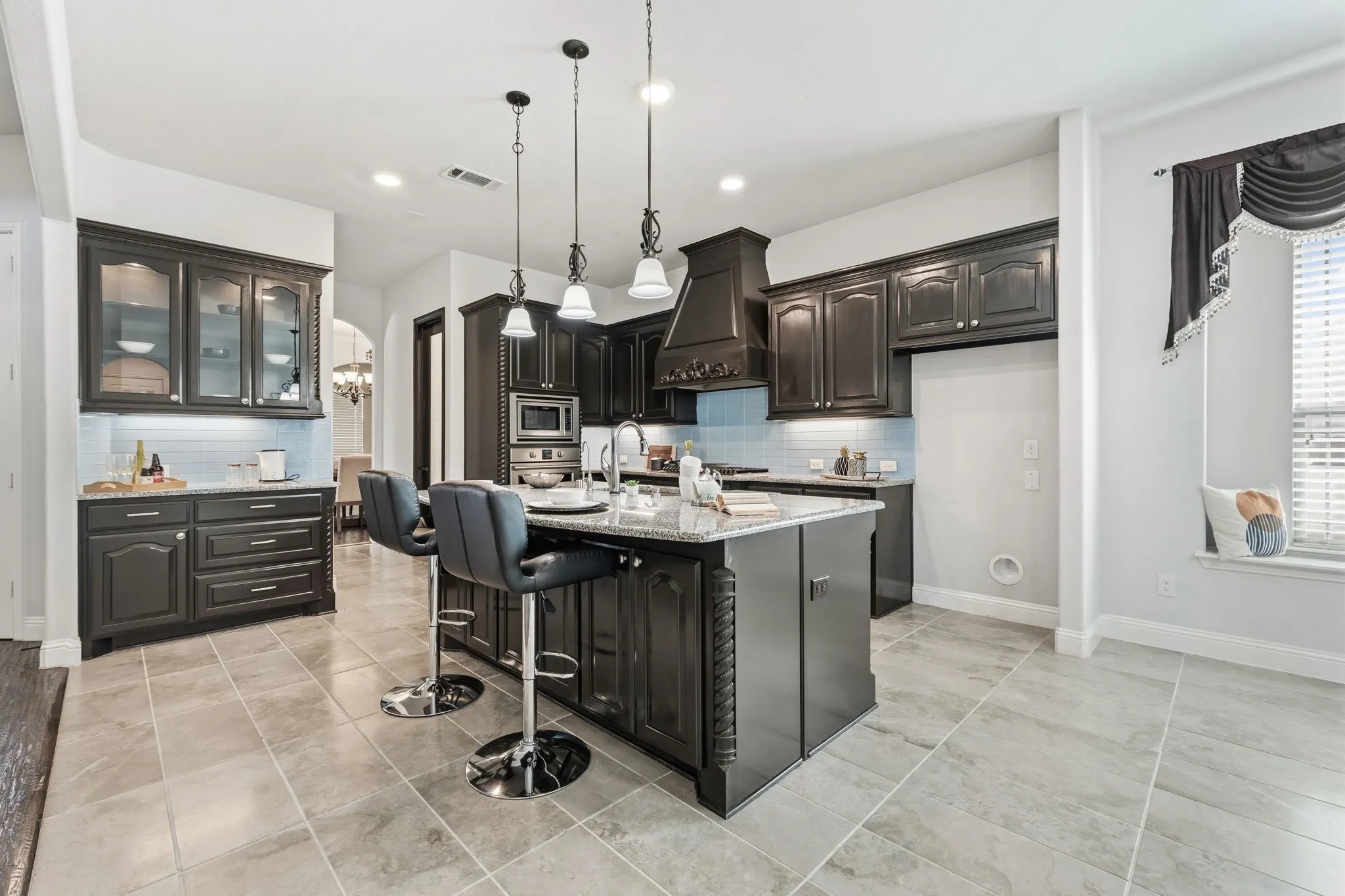 Kitchen featuring dark wood-finish cabinetry, a large central island with granite countertop, stainless steel appliances, a light blue tile backsplash, and recessed lighting