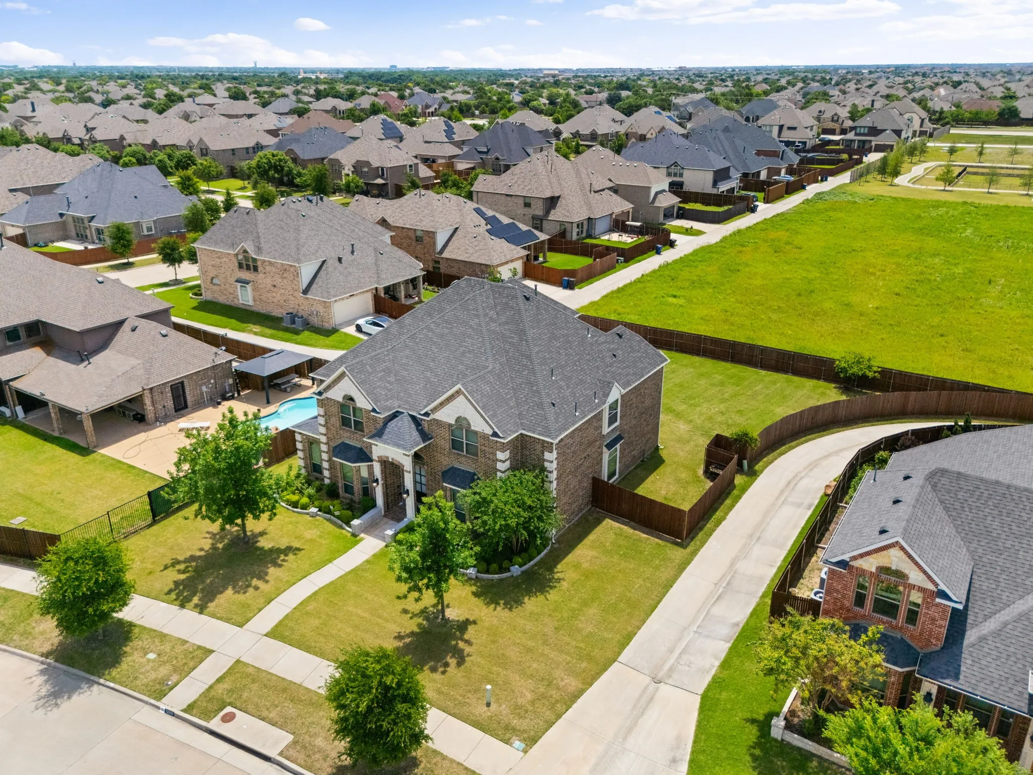 Brick and stone residence with a dark shingle roof, featuring a private swimming pool, mature landscaping, and an attached two-car garage
