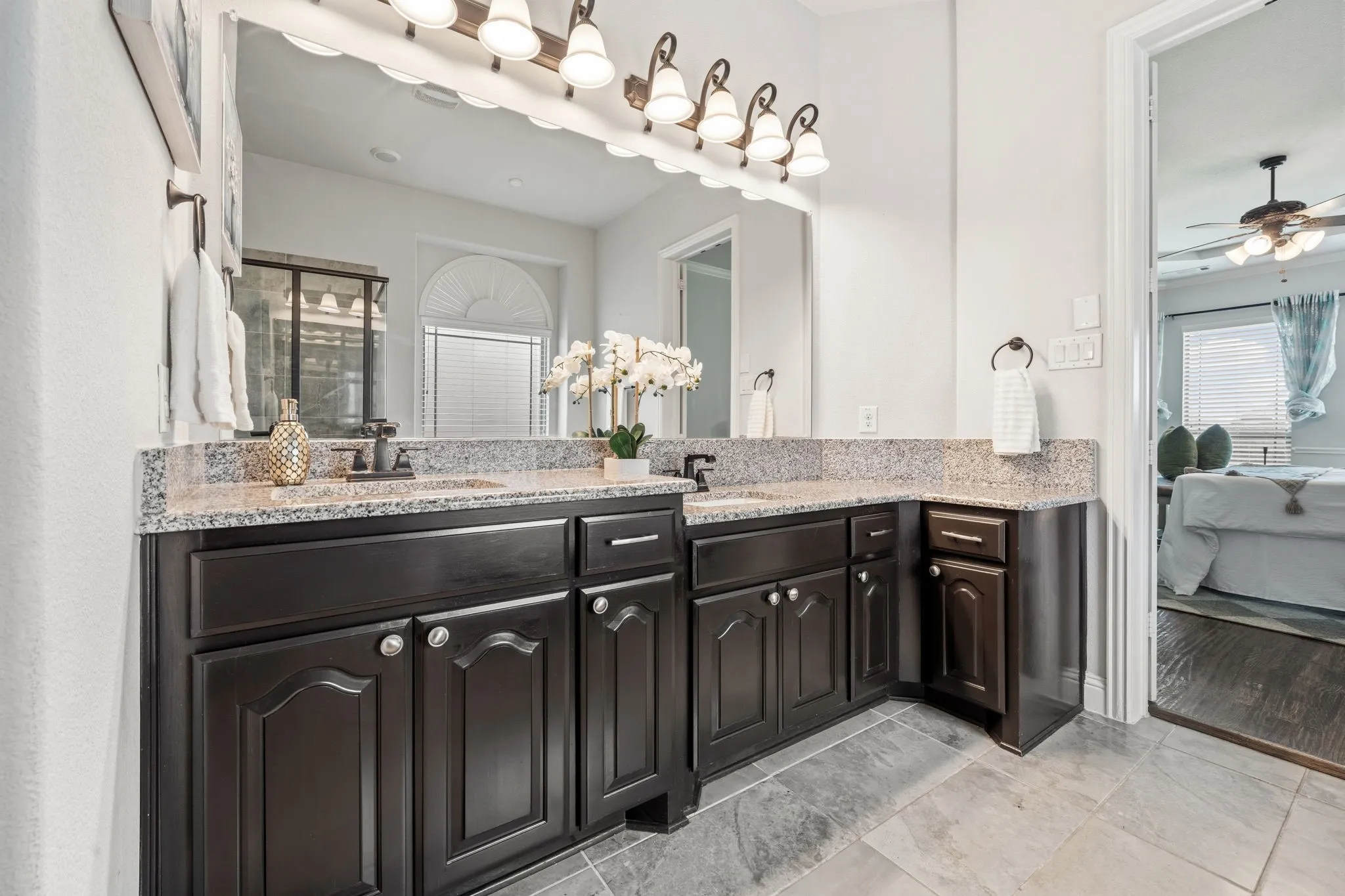Dual vanity with dark wood cabinetry, light speckled countertop, and modern black fixtures