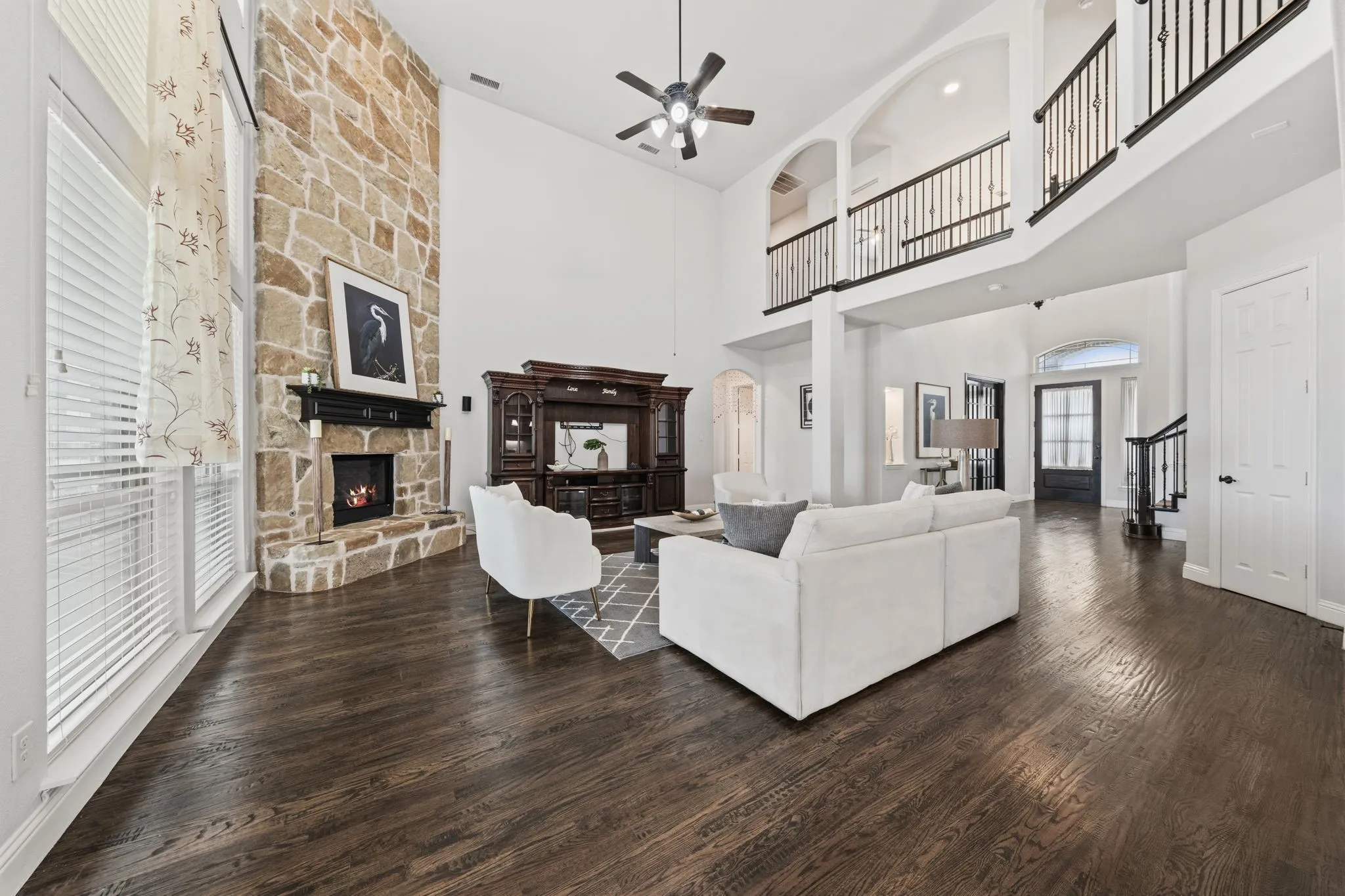 Vaulted living space featuring a floor-to-ceiling stone fireplace, dark wood-finish flooring, and a second-story balcony with wrought iron railing