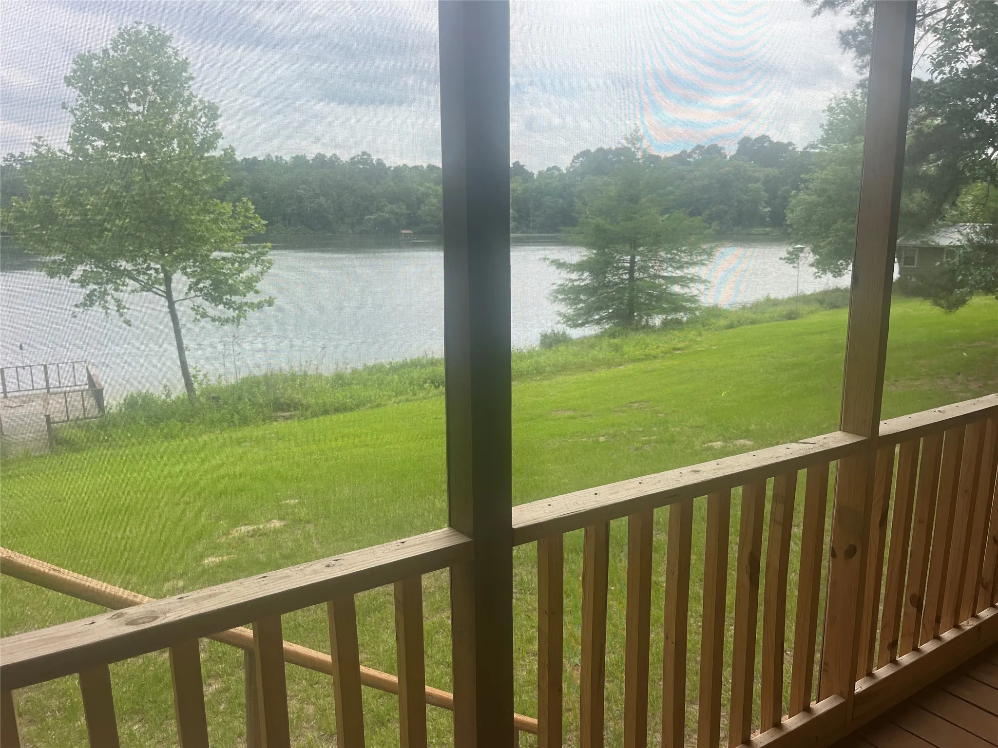 Screened porch with natural wood railing and flooring, providing water frontage with a dock