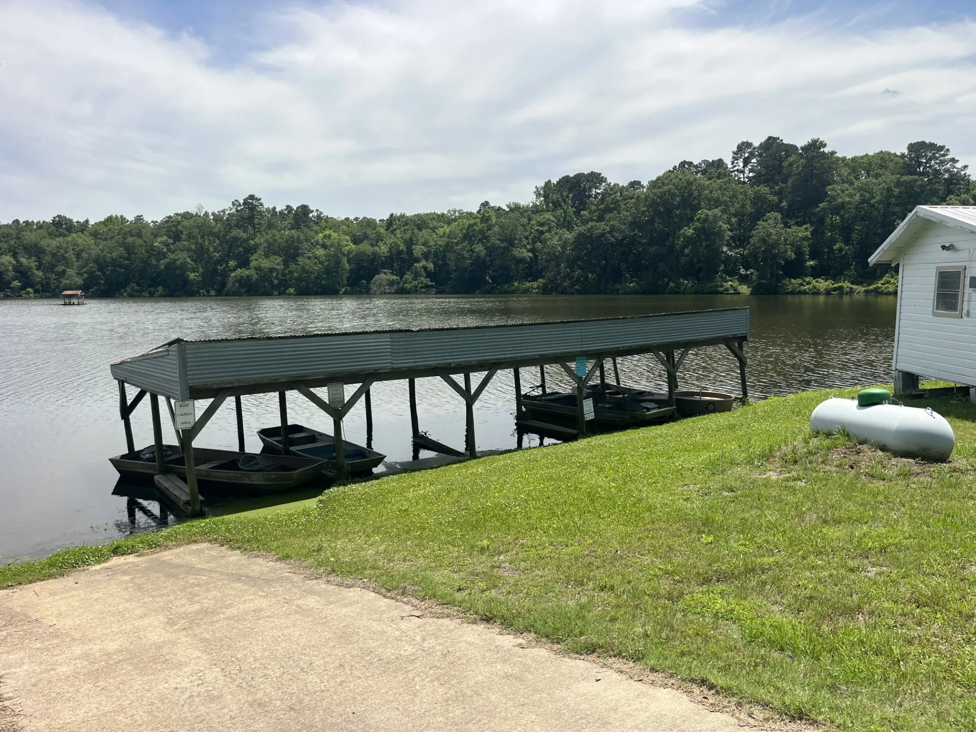 Waterfront property featuring a covered boat dock, direct water access, a level concrete pad, and a mature tree line backdrop