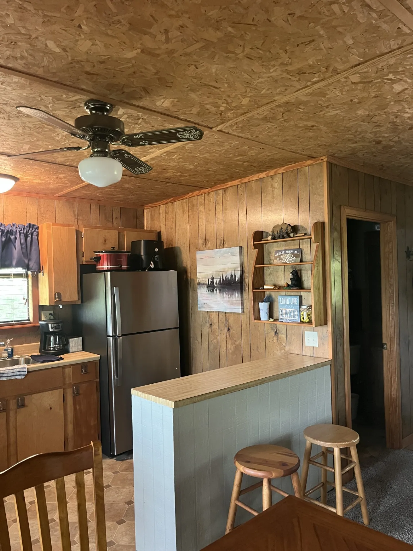Kitchen area featuring wood-finish wall paneling, ceiling fan with light kit, and stainless steel refrigerator