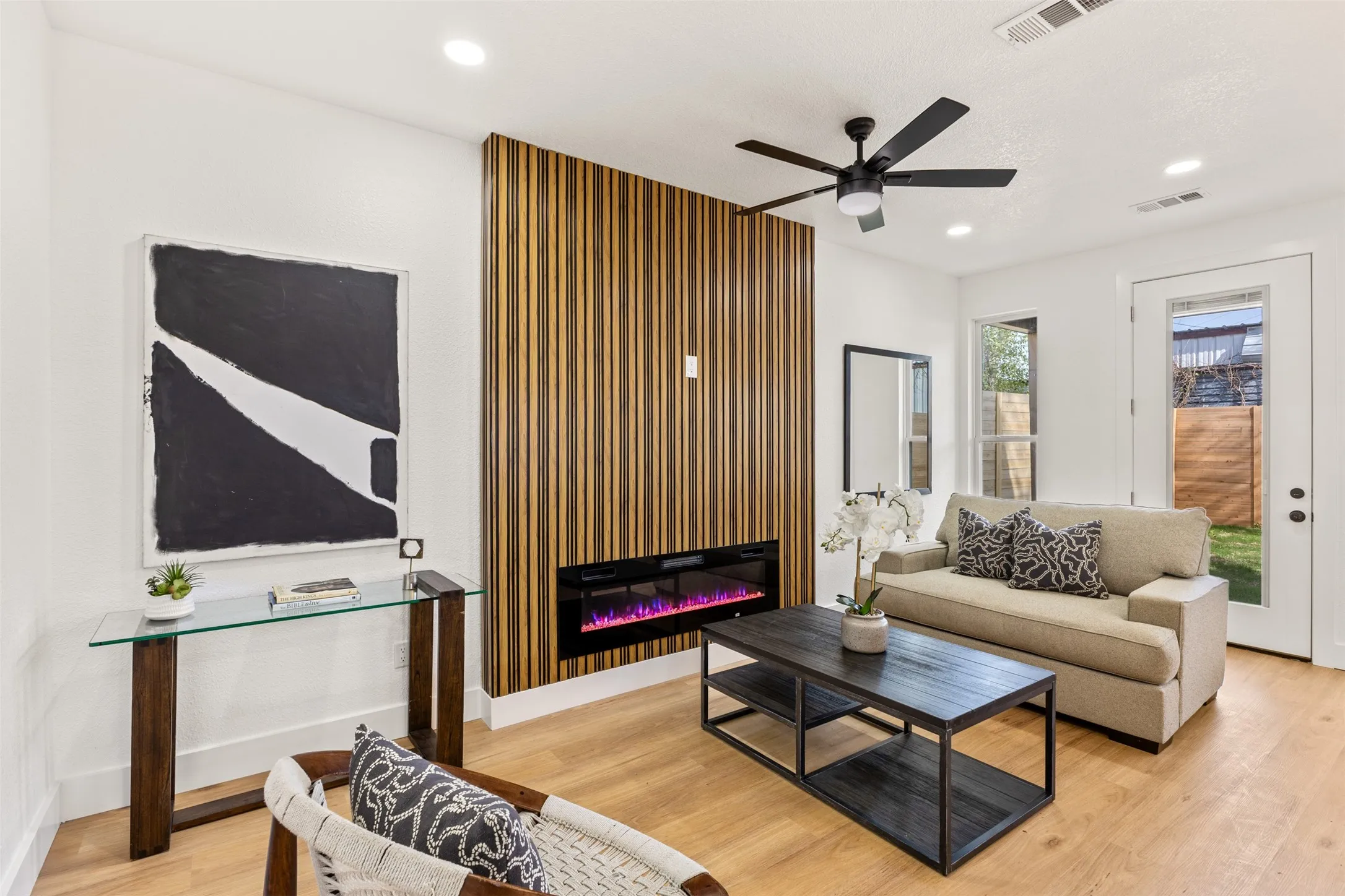 Living room with light wood-type flooring, ceiling fan, a glass covered fireplace, and recessed lighting