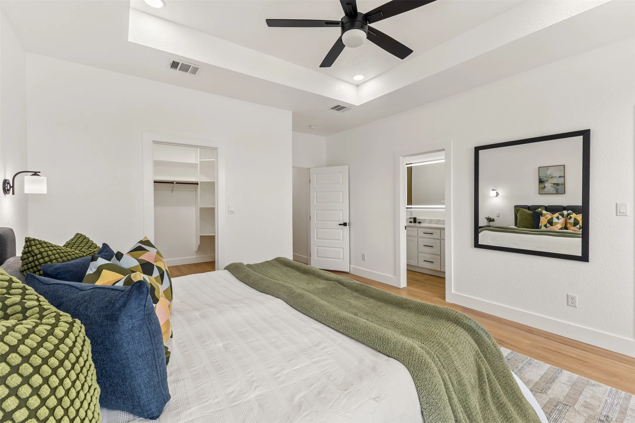 Bedroom with a tray ceiling, a spacious closet, a ceiling fan, light wood finished floors, and recessed lighting