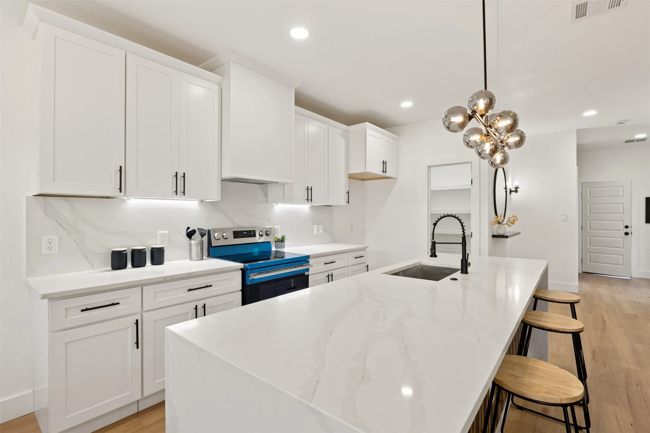 Kitchen with stainless steel electric range oven, light wood finished floors, white cabinetry, light stone counters, and a center island with sink
