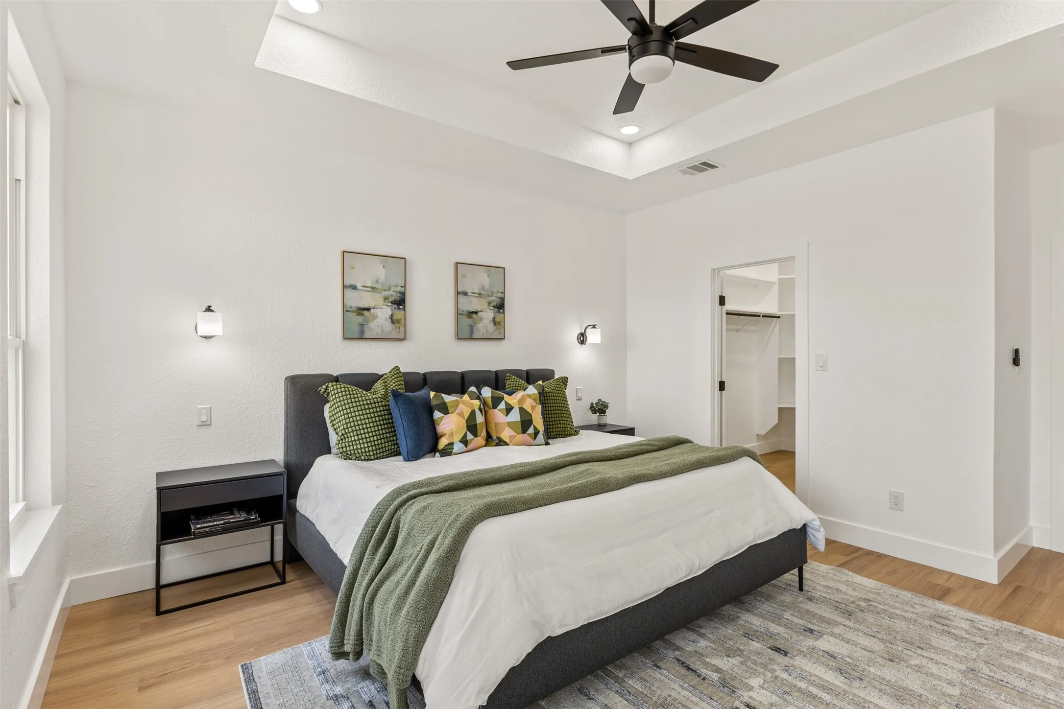 Bedroom with a raised ceiling, light wood-style floors, a walk in closet, a ceiling fan, and recessed lighting