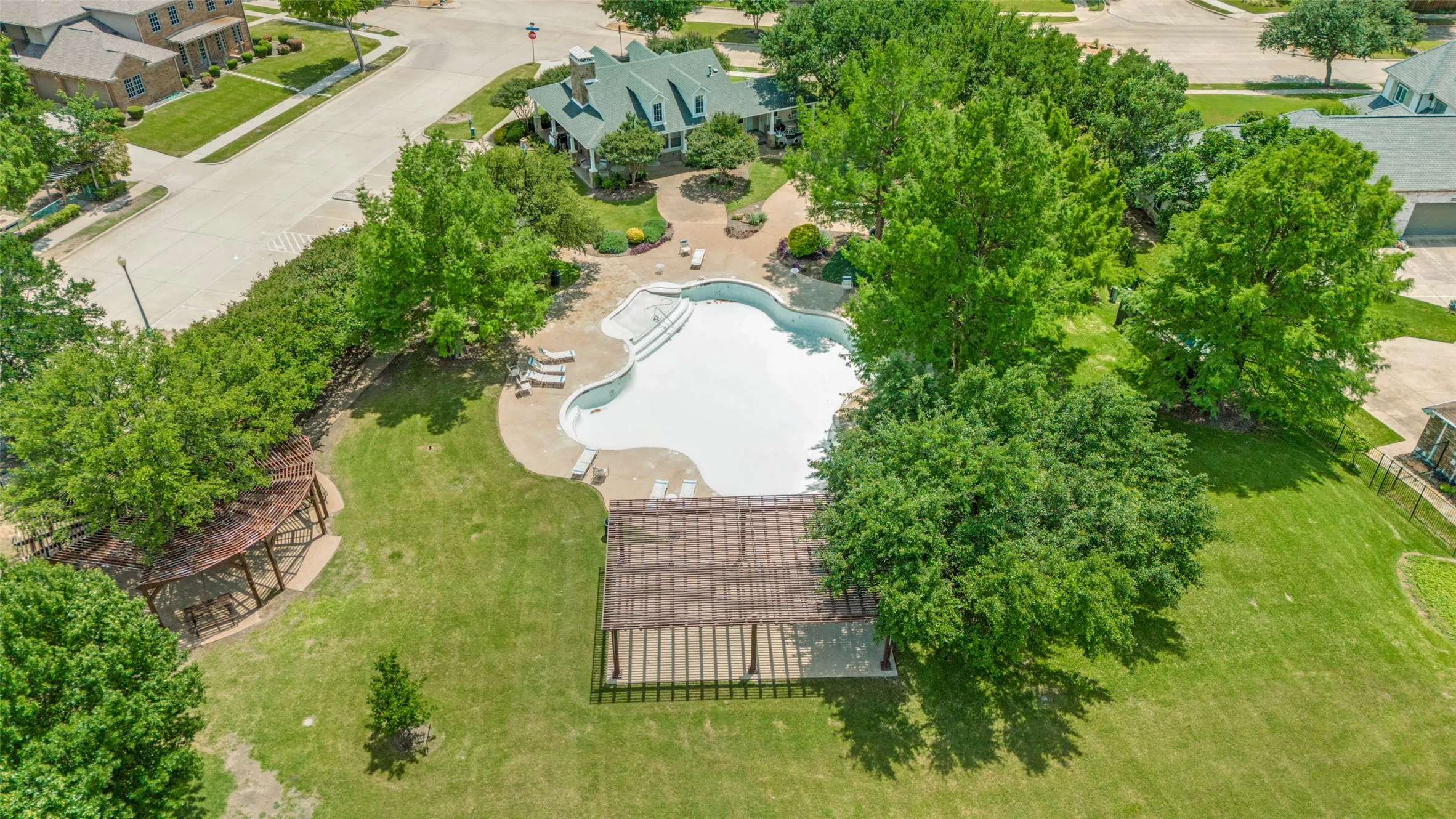 Expansive club house backyard featuring a large swimming pool with integrated steps, concrete patio surround, and two distinct pergola structures.