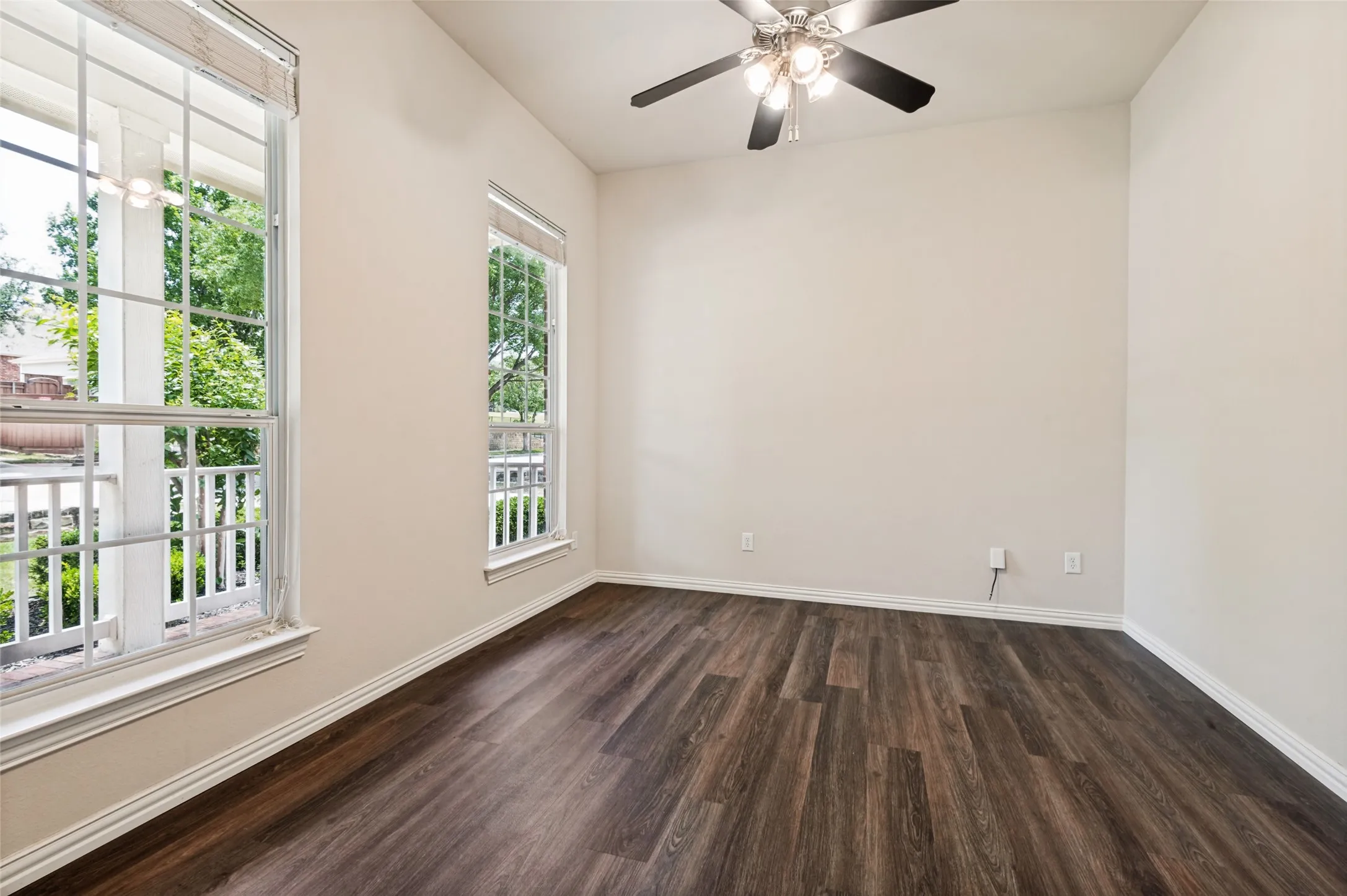 Spacious room featuring wood-finish flooring, neutral-toned walls, and a ceiling fan with integrated lighting. Great views of your front cottage garden!