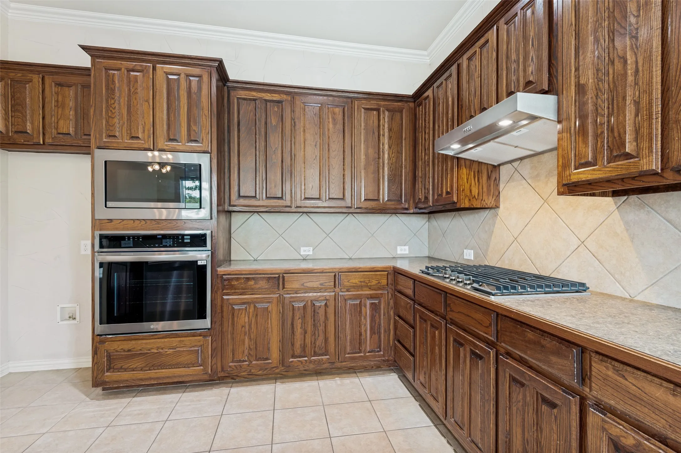 Kitchen featuring extensive (did you notice extensive??) wood cabinetry, stainless steel built-in microwave and oven, a gas cooktop with a coordinating range hood, and tile flooring.