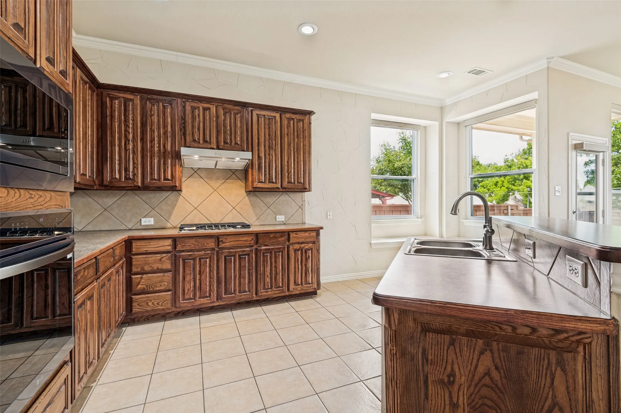 Kitchen with abundance of wood cabinetry, tile flooring, built-in stainless steel appliances, a gas cooktop with ventilation hood, and a double basin sink
