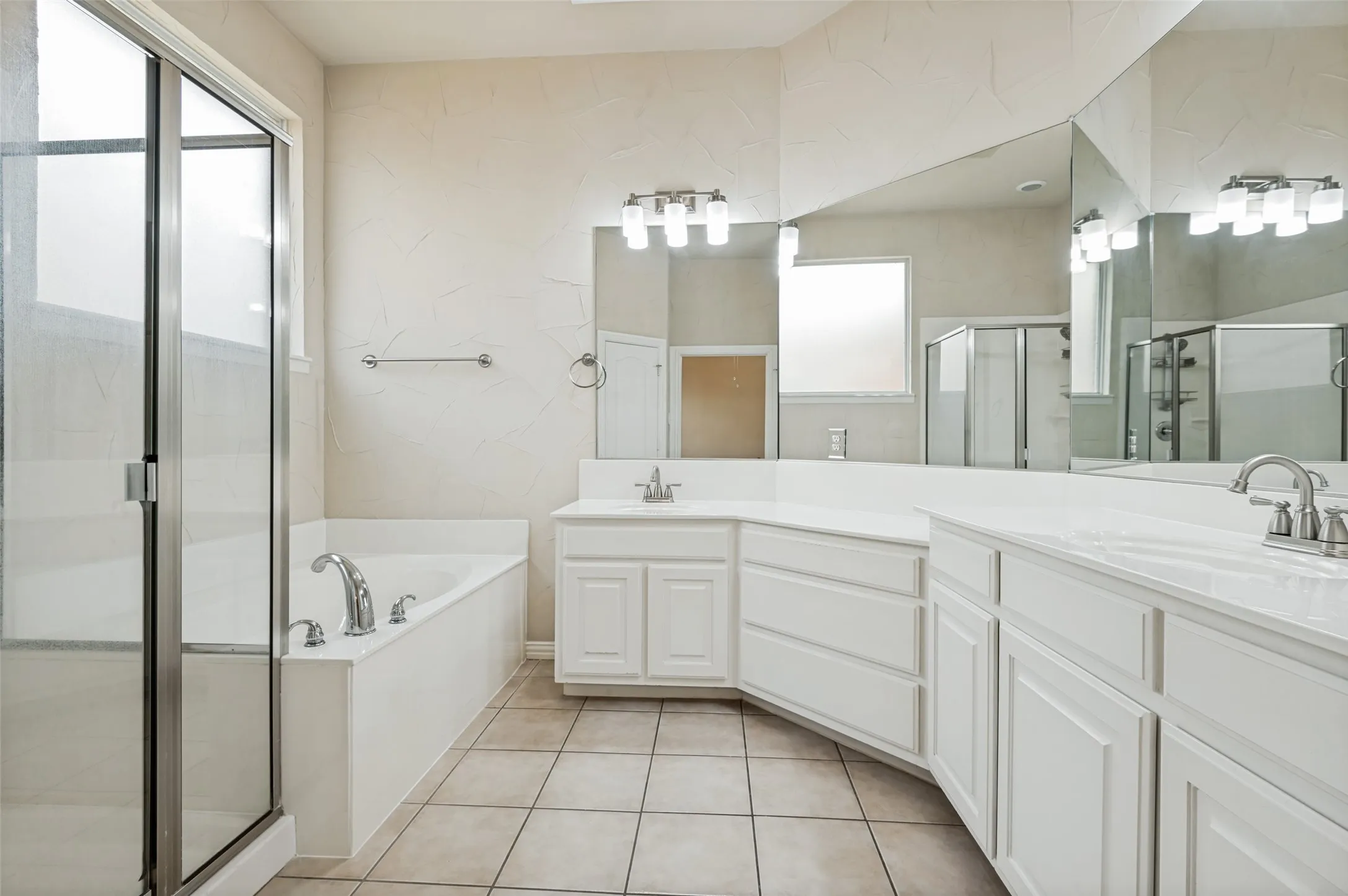 Love the surround mirror feature! Bathroom has a glass-enclosed shower, a built-in garden tub with chrome fixtures, dual vanity sinks with chrome faucets, white cabinetry, and large format floor tiling. Linen closet and separate enclosed water closet.