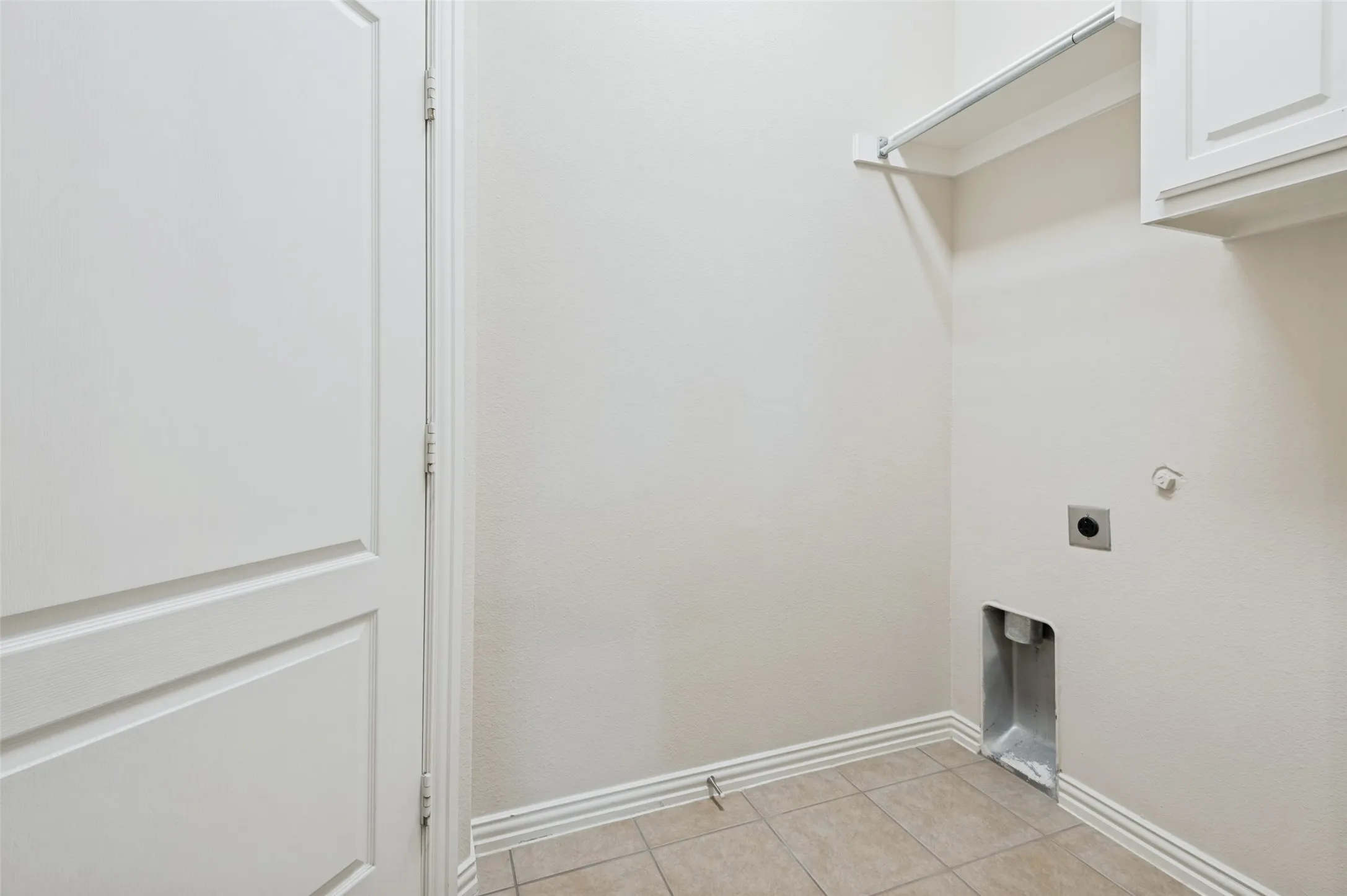 Utility area featuring neutral walls, tiled flooring, built-in shelving, and upper cabinetry. Love the hanging space!  Convenient entry from garage.