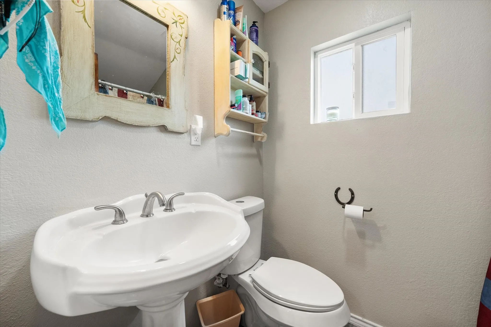 Pedestal sink with brushed nickel faucet, mirror with decorative frame, recessed window, and wall-mounted shelving