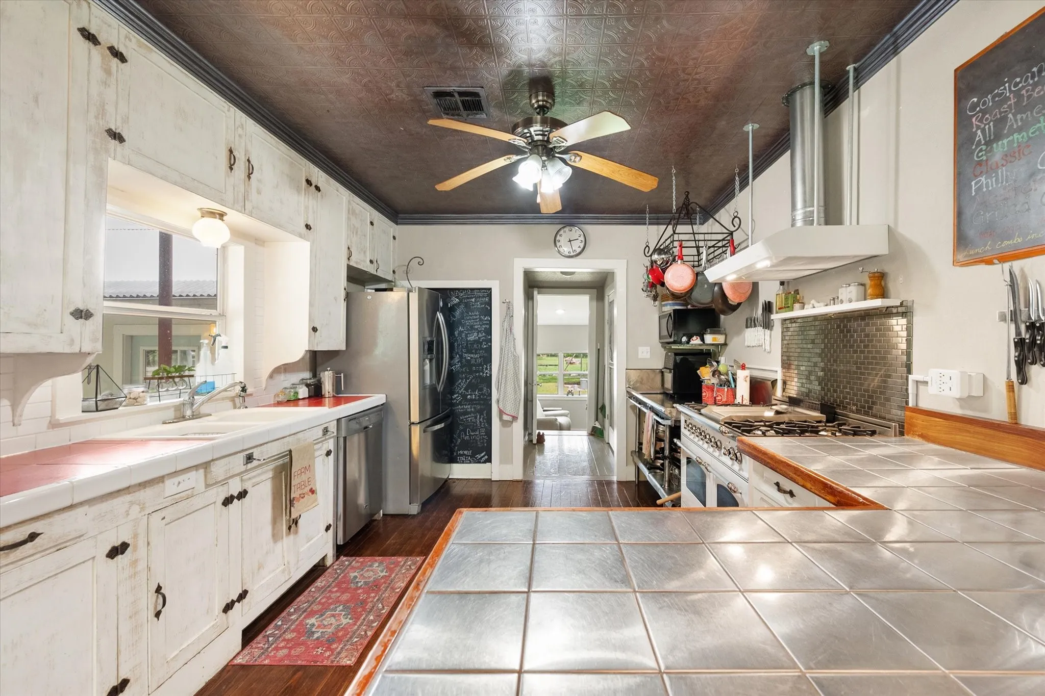 Kitchen featuring distressed white cabinetry, pressed tin ceiling, wood-finish flooring, stainless steel appliances, and a tile countertop island with a wood edge