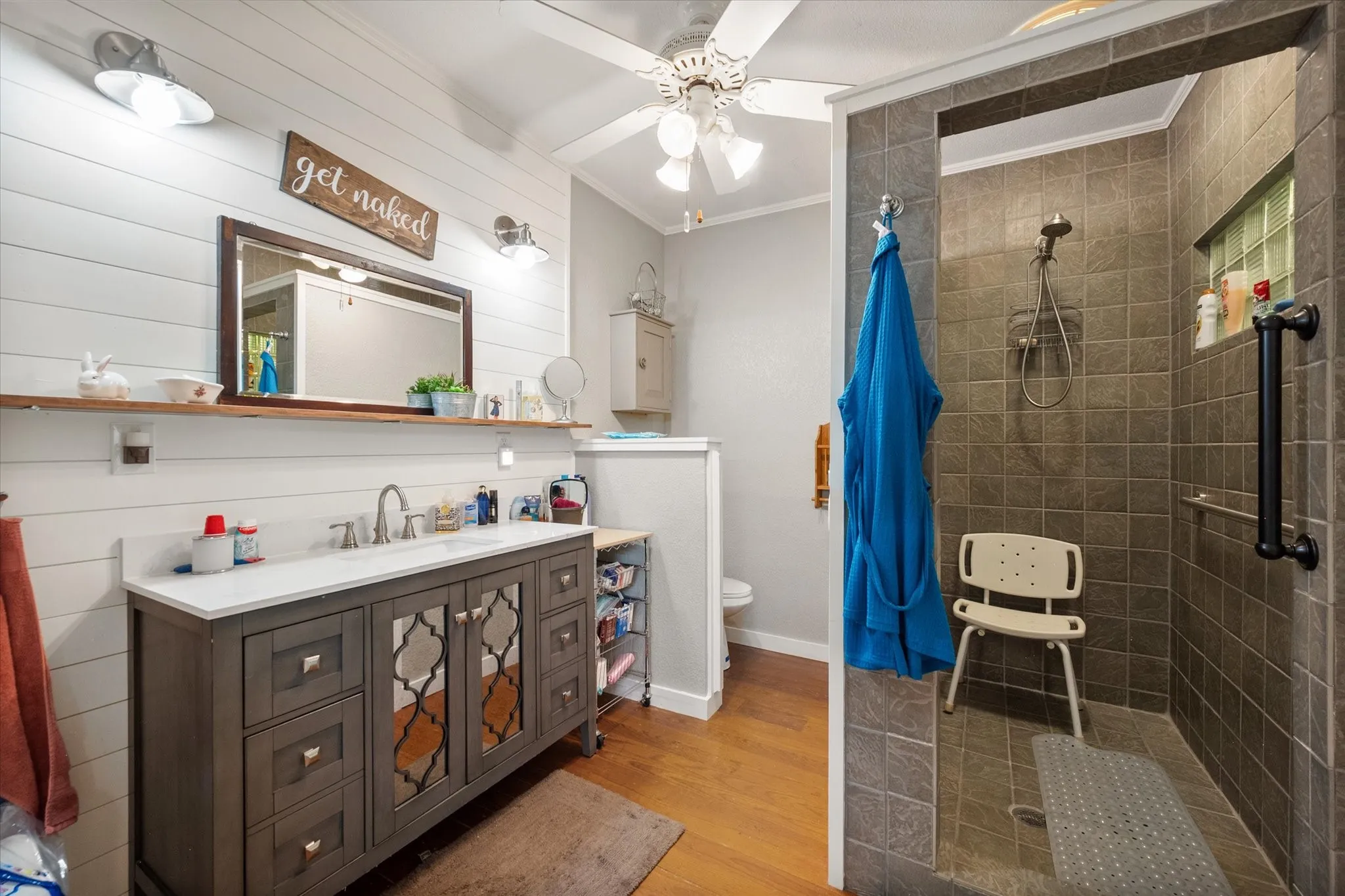 Spacious bathroom featuring a walk-in shower with tile surround and grab bars, a single vanity with storage, and wood-finish flooring