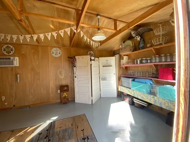 Interior featuring exposed wood beam ceiling, plywood paneling, wall-mounted air conditioning unit, and built-in shelving