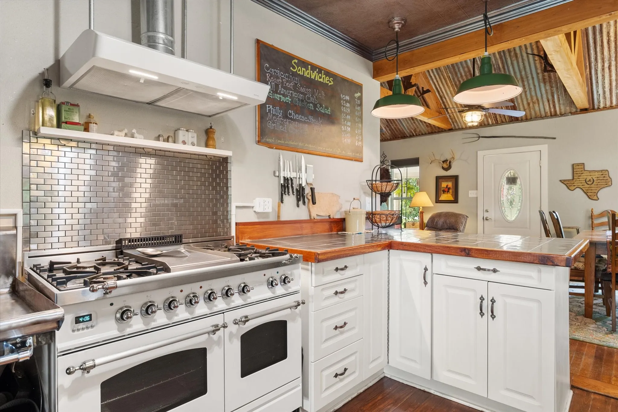 Gourmet kitchen featuring a professional-grade range, white cabinetry, wood-finish countertops, subway tile backsplash, and a corrugated metal ceiling
