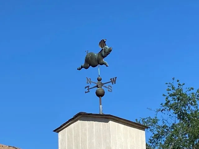 Cupola-mounted weathervane featuring a decorative pig figurine and directional indicators