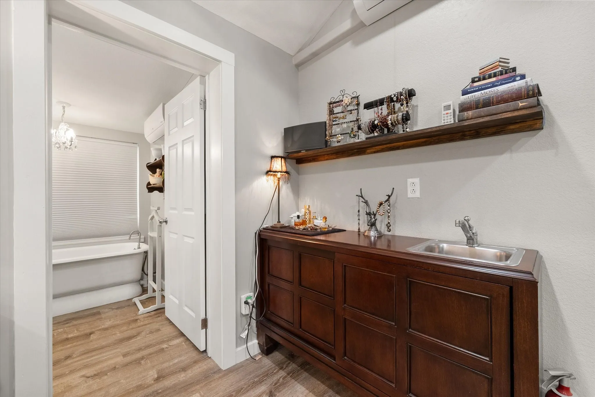 Warm wood-finish flooring complements the freestanding soaking tub, illuminated by a decorative chandelier