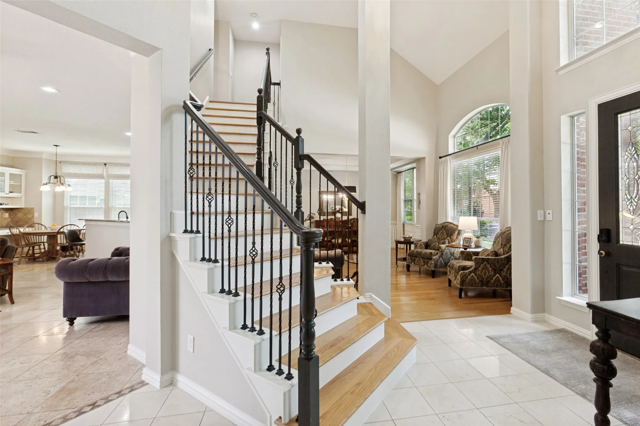 Foyer with tile flooring featuring a decorative border, a prominent staircase with wood treads and wrought iron balusters, and an arched window providing natural illumination