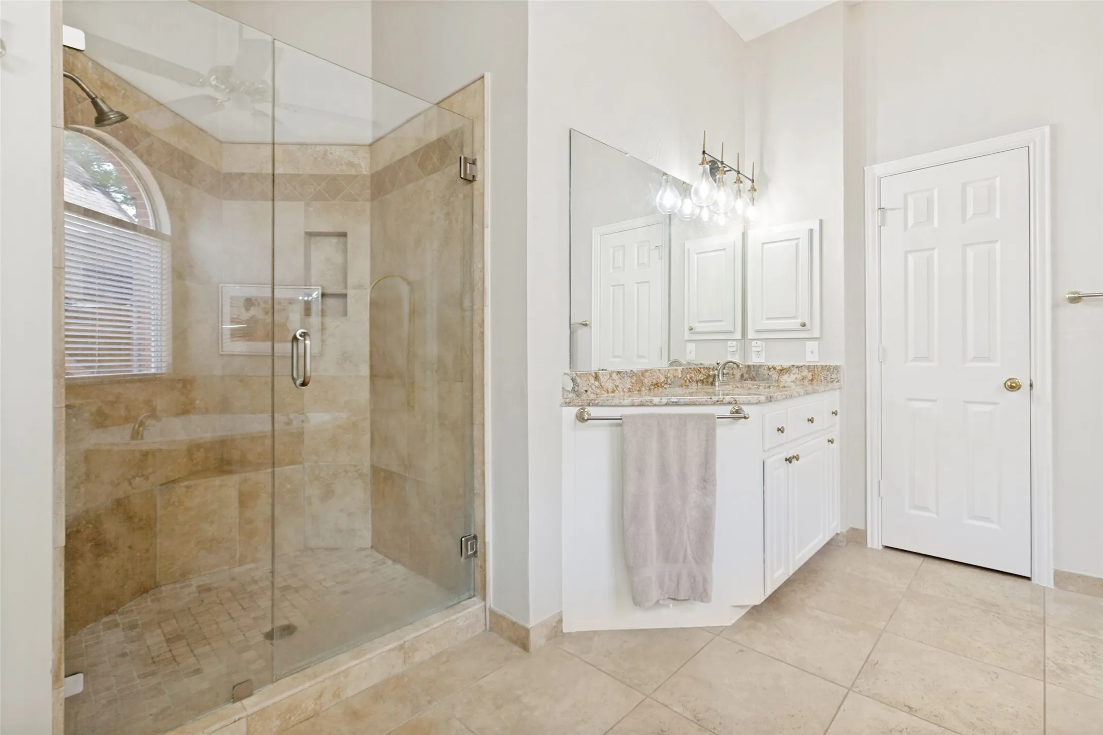 Spacious bathroom featuring a glass-enclosed shower with stone tile, an arched window, and a built-in bench