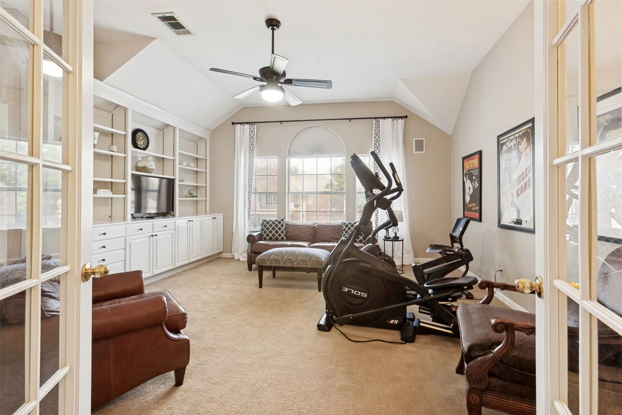French doors opening to a versatile room featuring extensive built-in cabinetry, arched windows, vaulted ceilings, and a ceiling fan