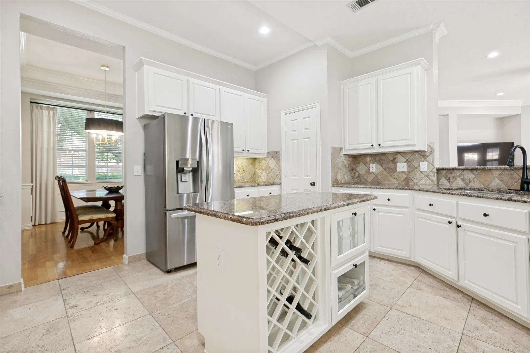 Kitchen with white cabinetry, stainless steel refrigerator, granite countertops, and tiled backsplash