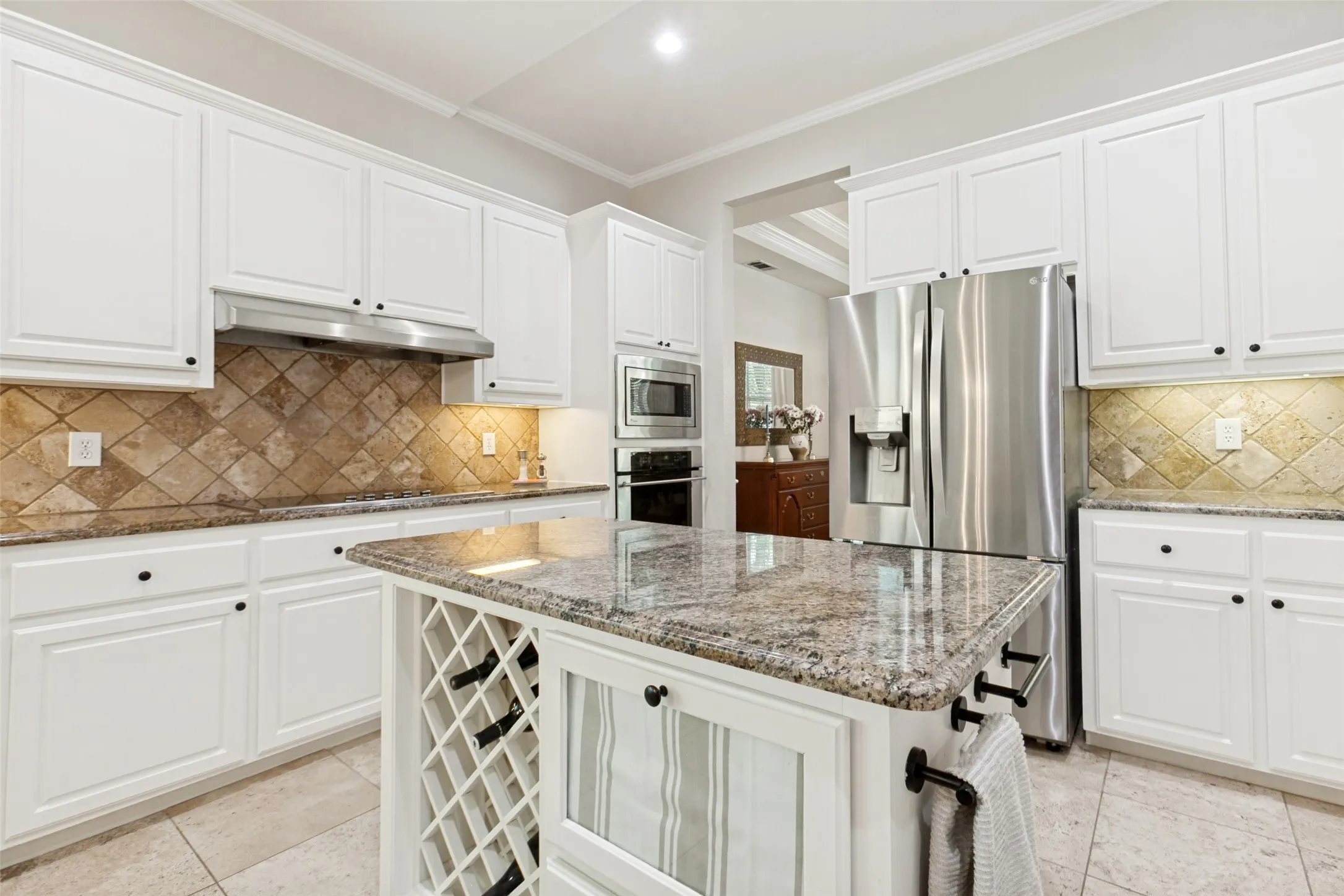 Spacious kitchen featuring white cabinetry, granite countertops, a diamond-patterned tile backsplash, stainless steel appliances, and a central island with integrated wine storage