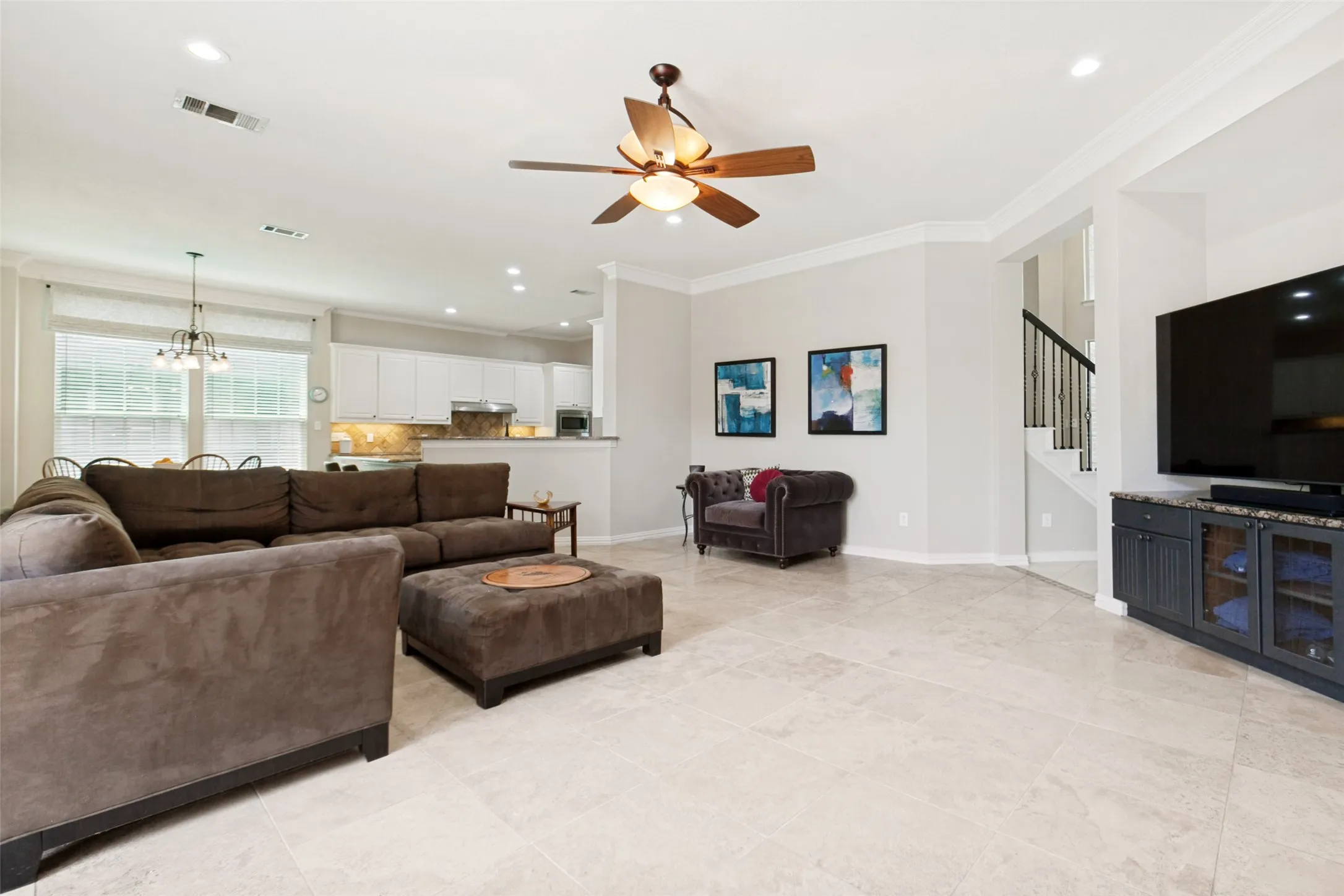 Spacious living area featuring light-toned tile flooring, recessed lighting, and crown molding