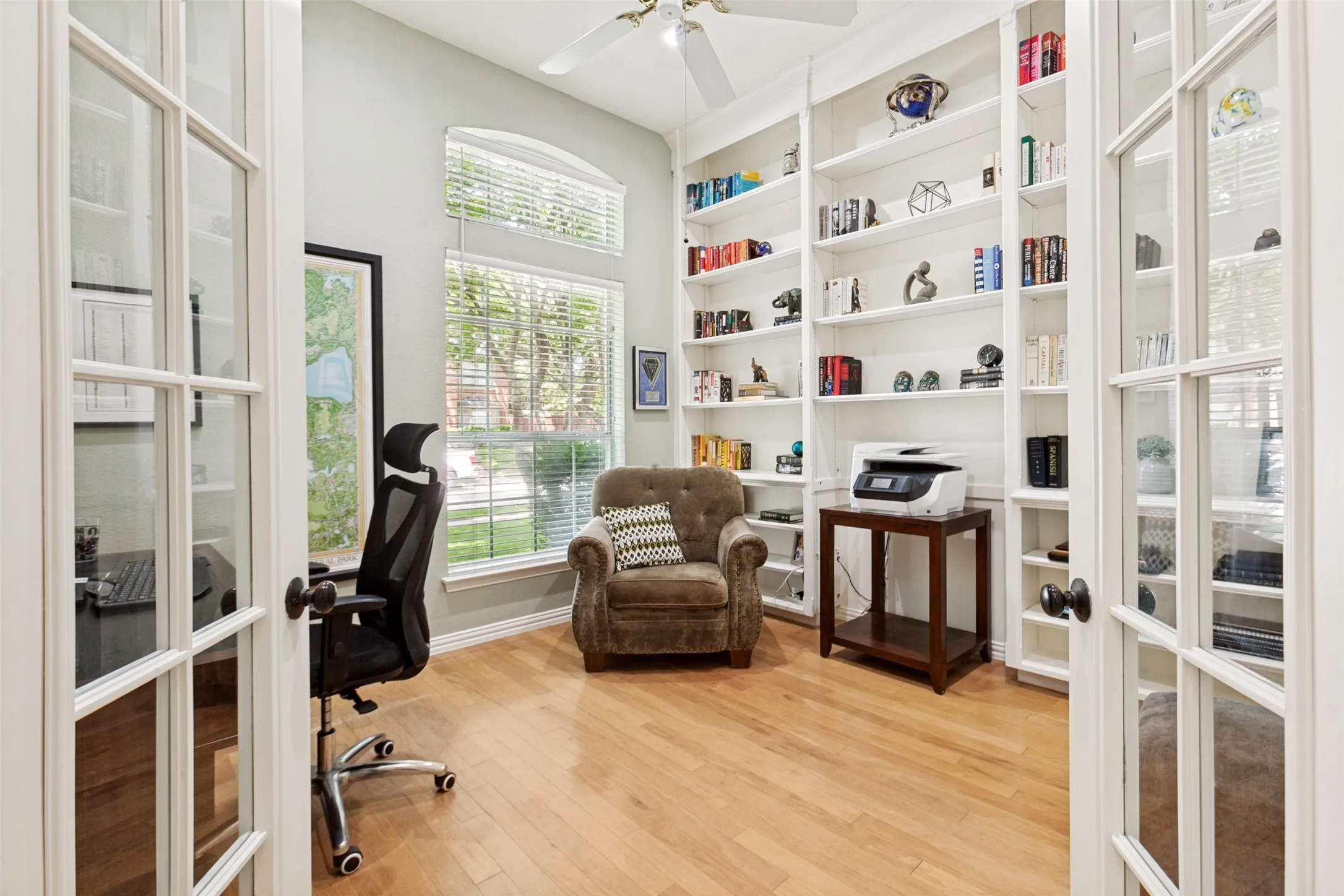 French doors open to a versatile room featuring extensive built-in shelving, wood-finish flooring, and multiple windows