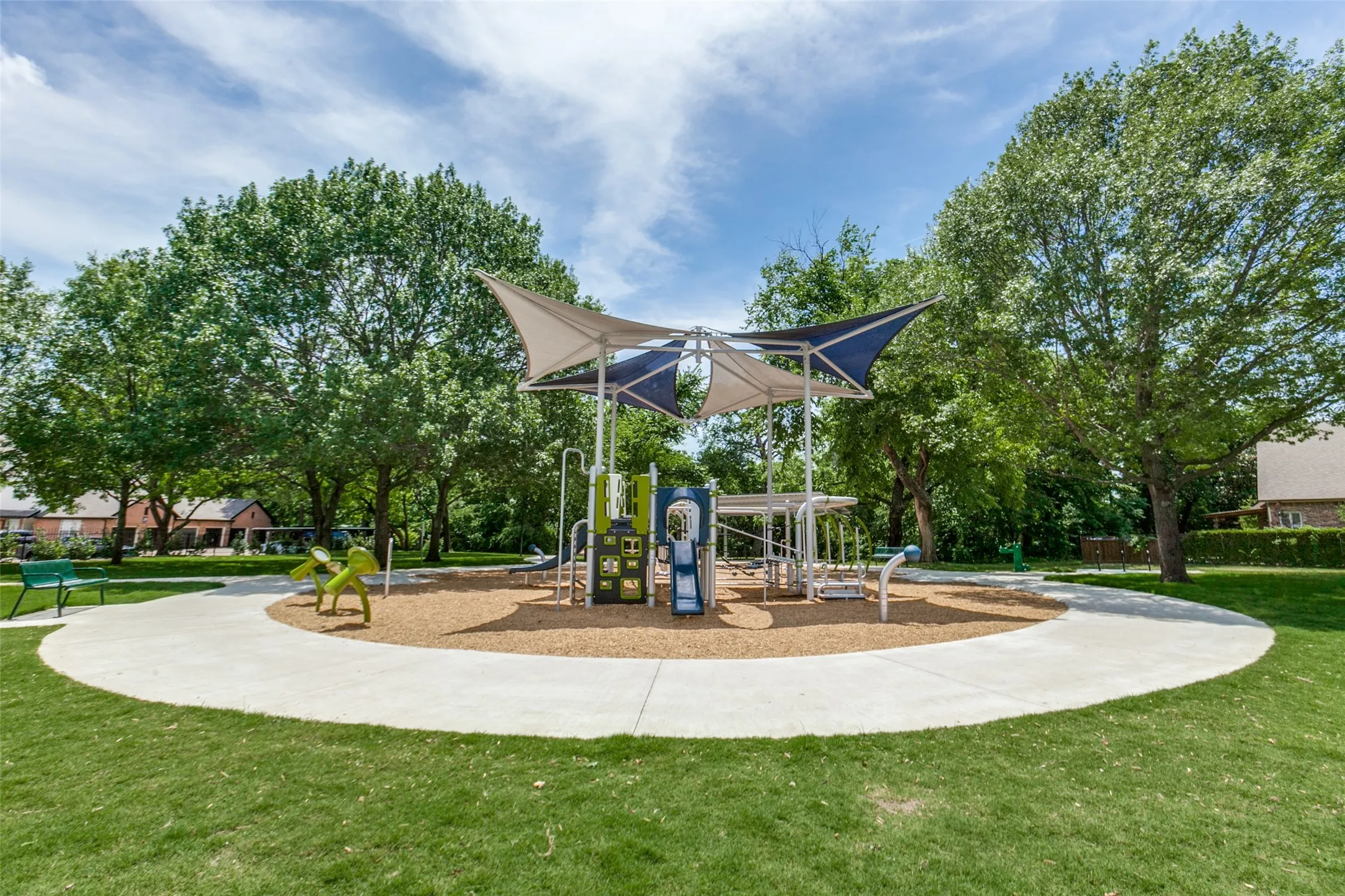 Community playground featuring a multi-level play structure with slides and climbing elements, shaded by a fabric canopy