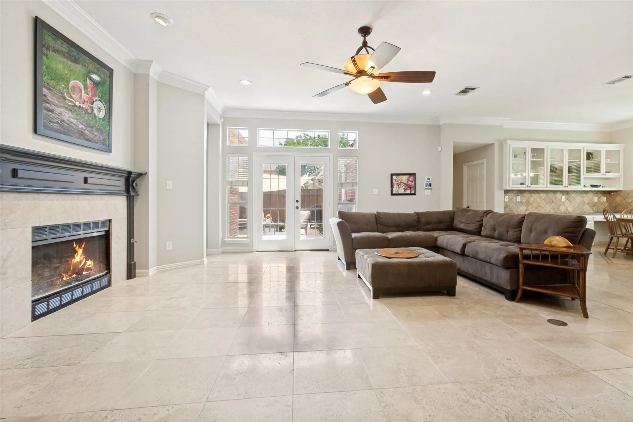 Spacious living area featuring light-toned tile flooring, a fireplace with a dark mantel, and multiple windows