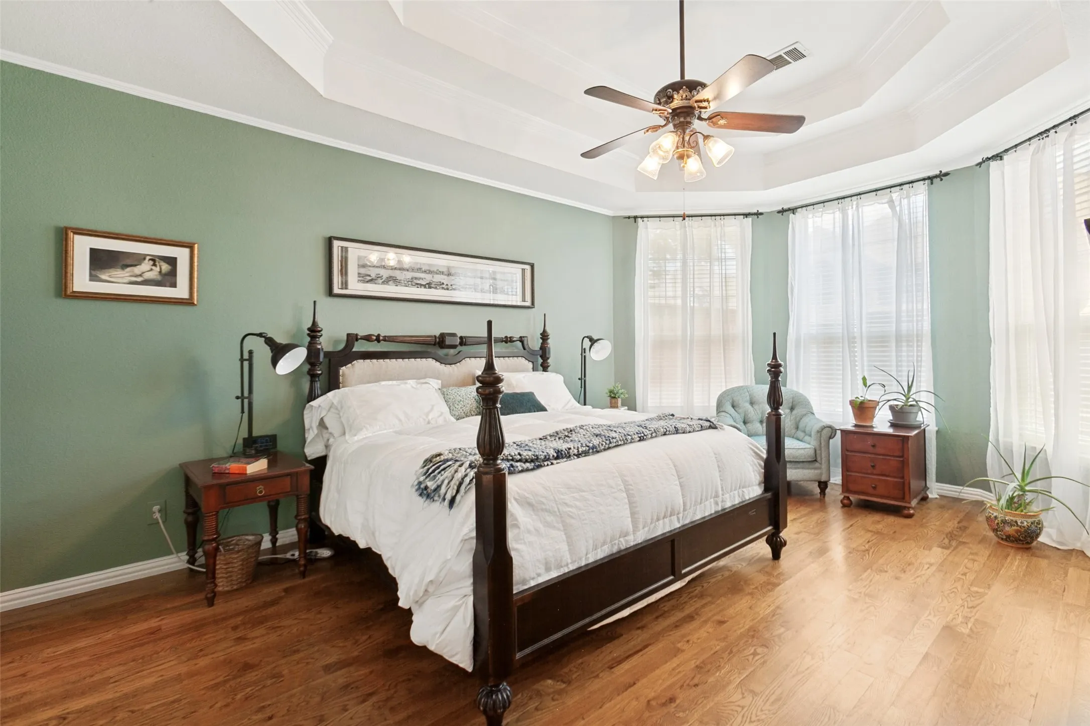 First floor primary bedroom suite featuring wood-finish flooring, a tray ceiling with crown molding, and a ceiling fan.