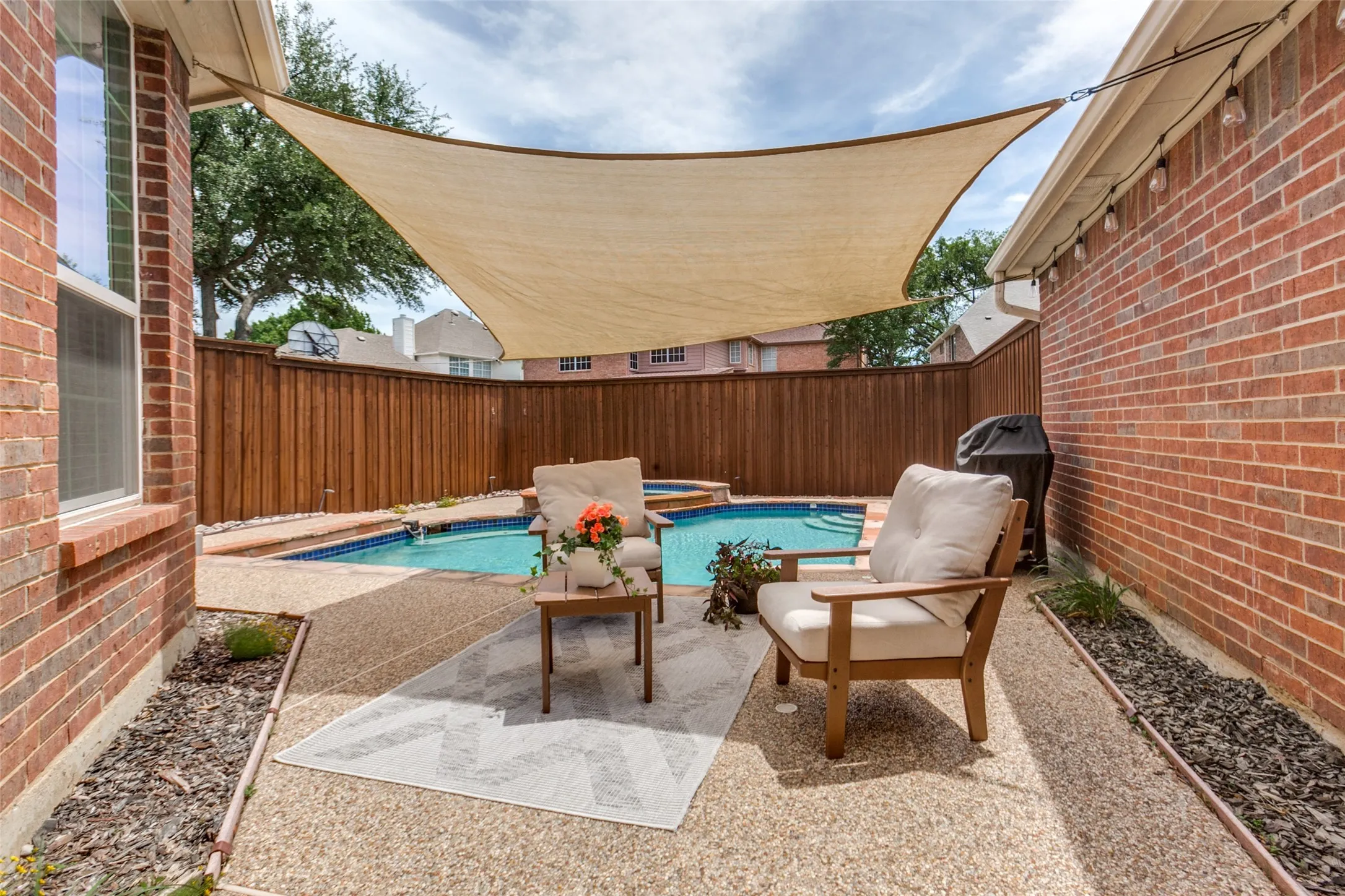 Backyard oasis featuring a swimming pool with integrated spa, a shade sail, and exposed aggregate patio