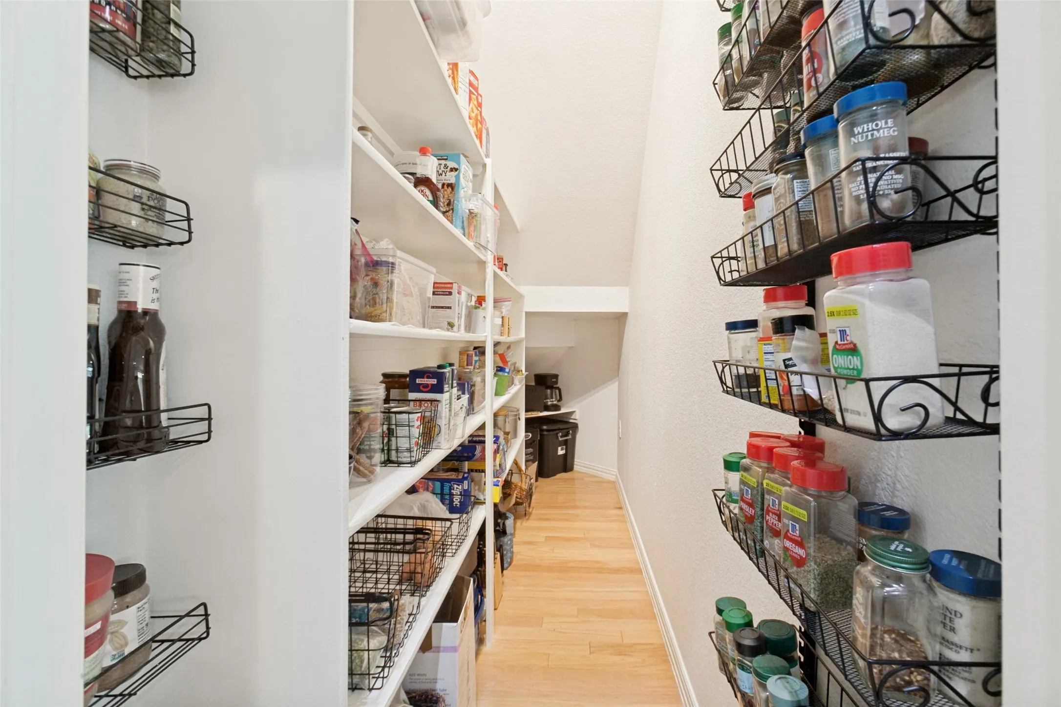 Spacious walk-in pantry featuring extensive built-in shelving, wall-mounted spice racks, and wood-finish flooring