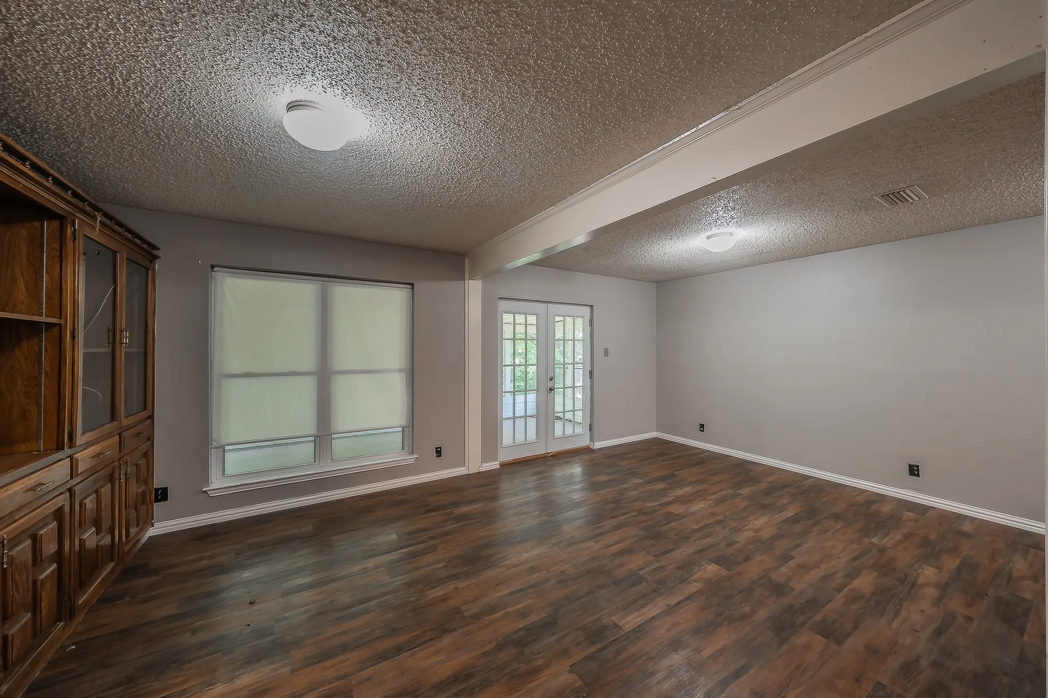 Spacious room with wood-finish flooring, light gray walls, and a textured ceiling