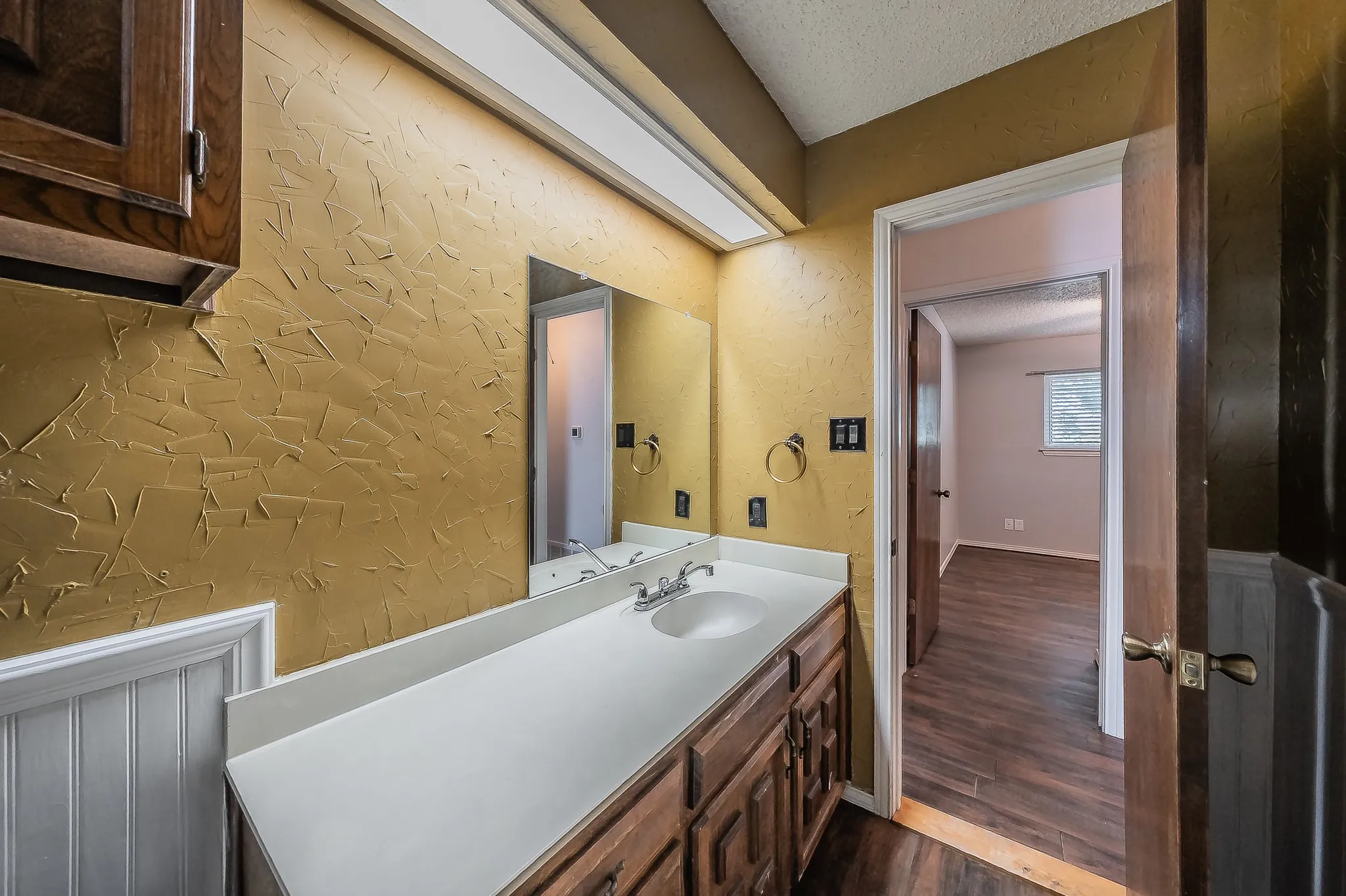 Bathroom vanity with integrated sink, wood-finish cabinetry, and white countertop