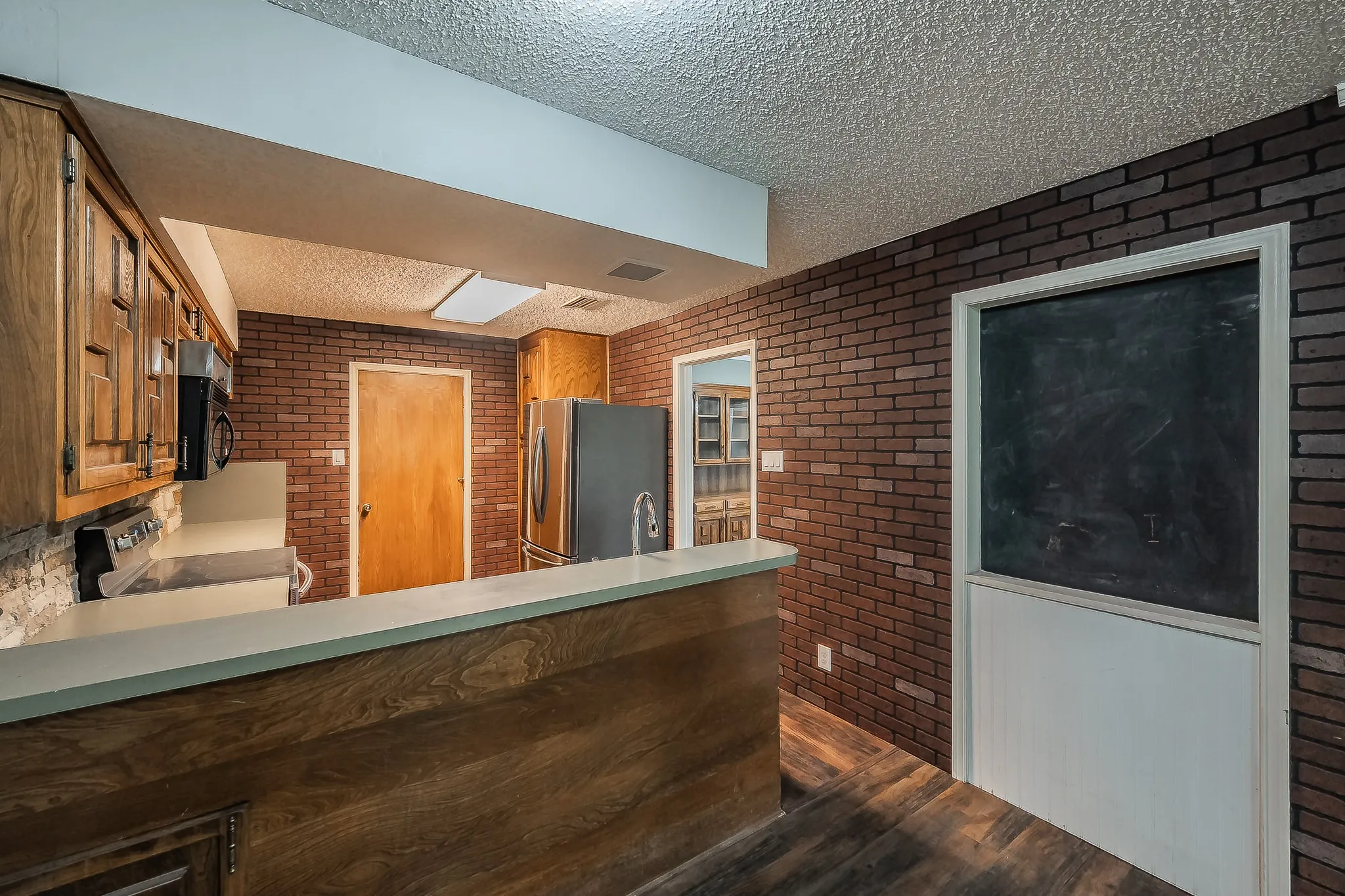 Kitchen area featuring wood-finish flooring and brick-patterned walls