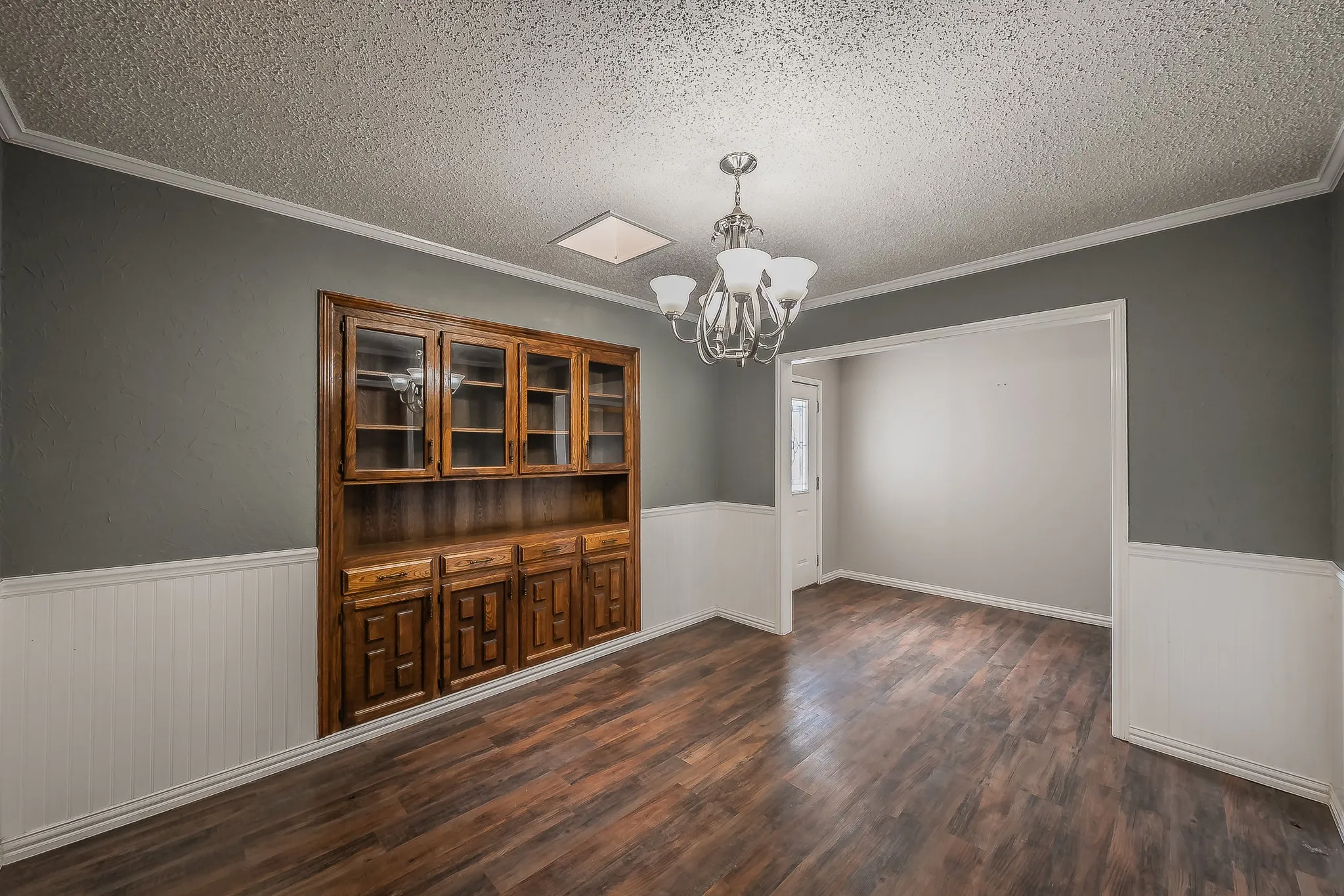 Open-concept room featuring wood-finish flooring, a built-in hutch with glass-front cabinetry, neutral wall paint, and white wainscoting